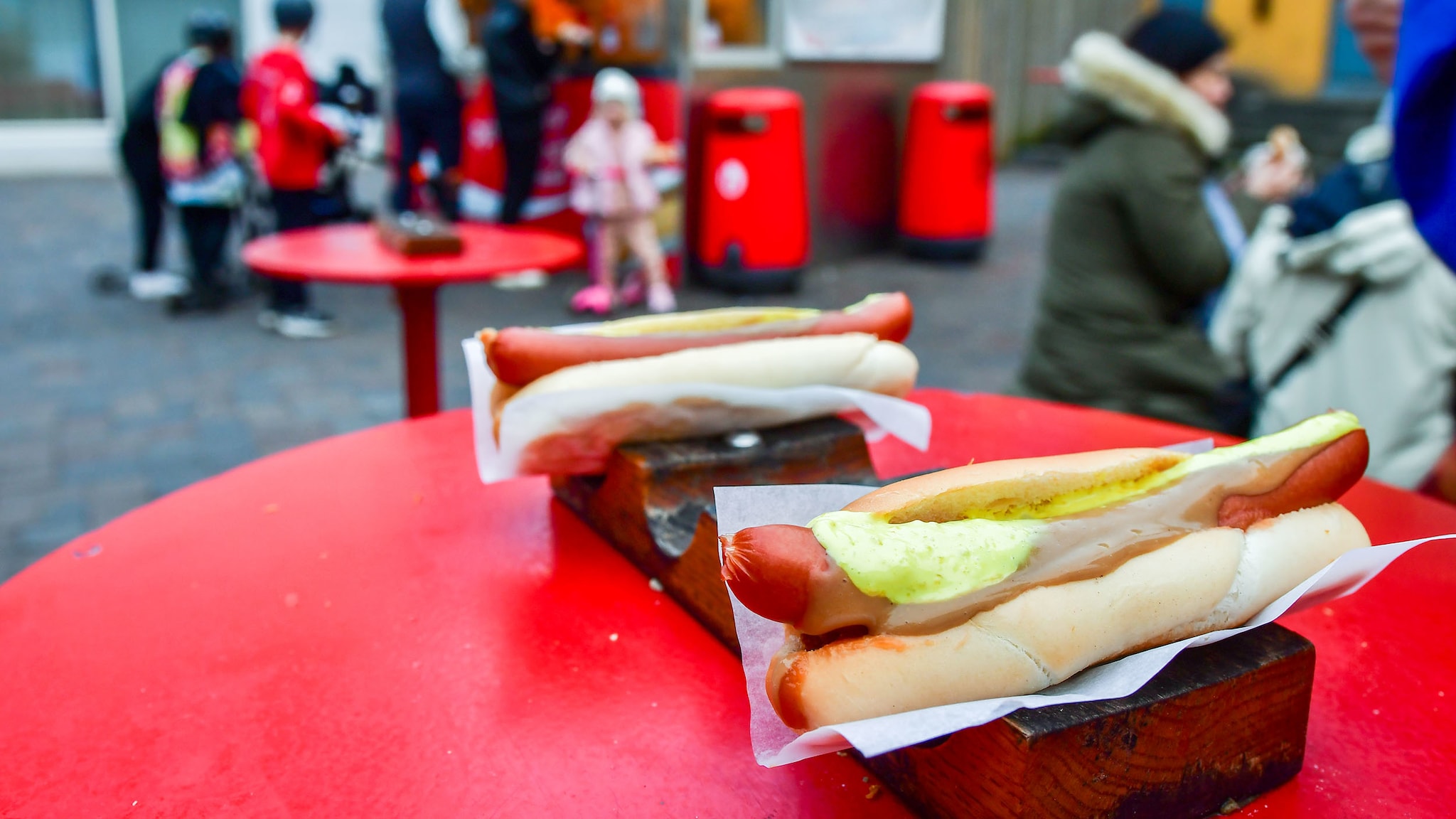 Zwei Hotdogs liegen auf einem Brett, das auf einem Tisch steht. 
