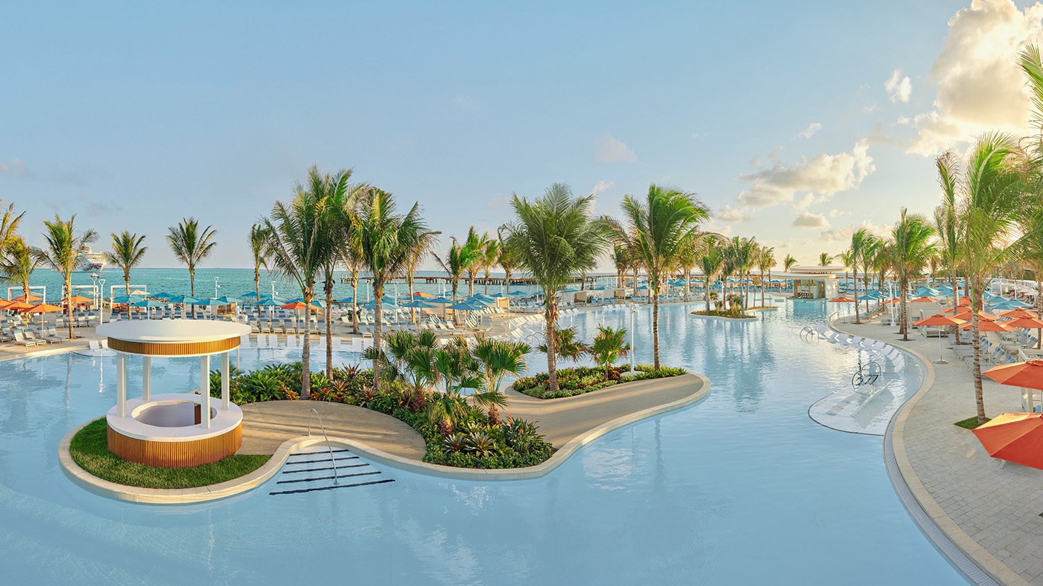 An einer Poollandschaft stehen Sonnenliegen neben Palmen.