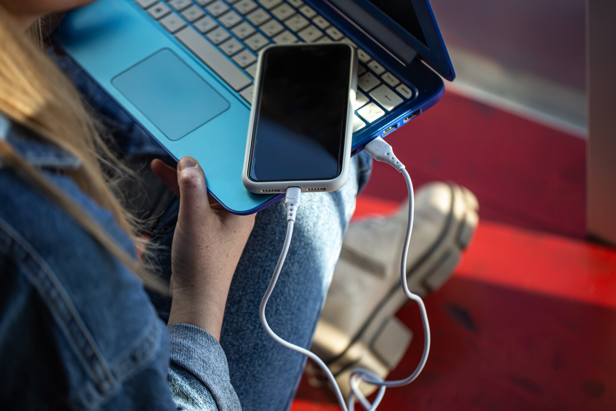 Eine Frau hat einen Laptop mit einem damit verbundenen Smartphone auf dem Schoß.
