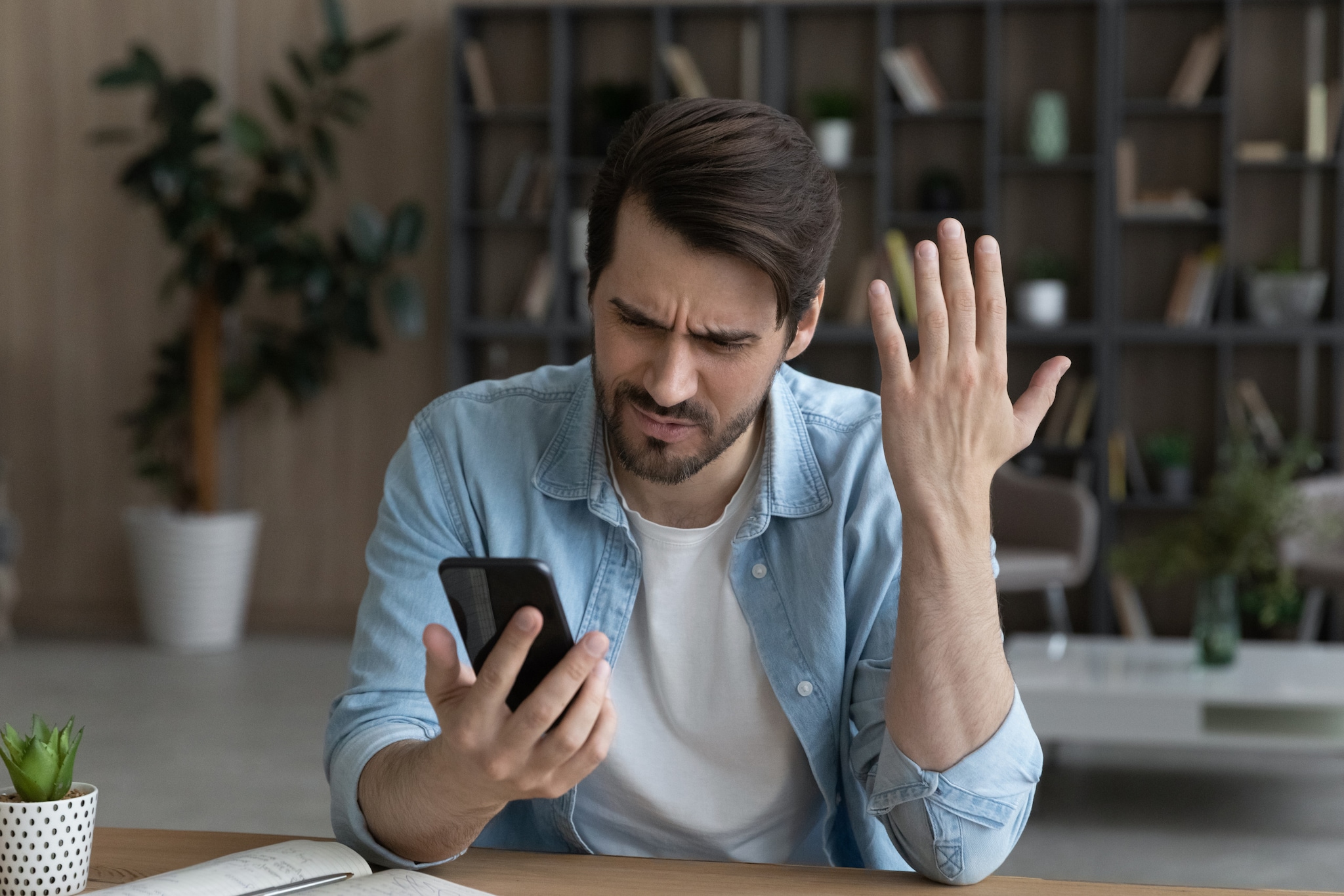 Ein Mann hält sein Smartphone in der Hand, schaut verärgert und hält die andere Hand hoch.