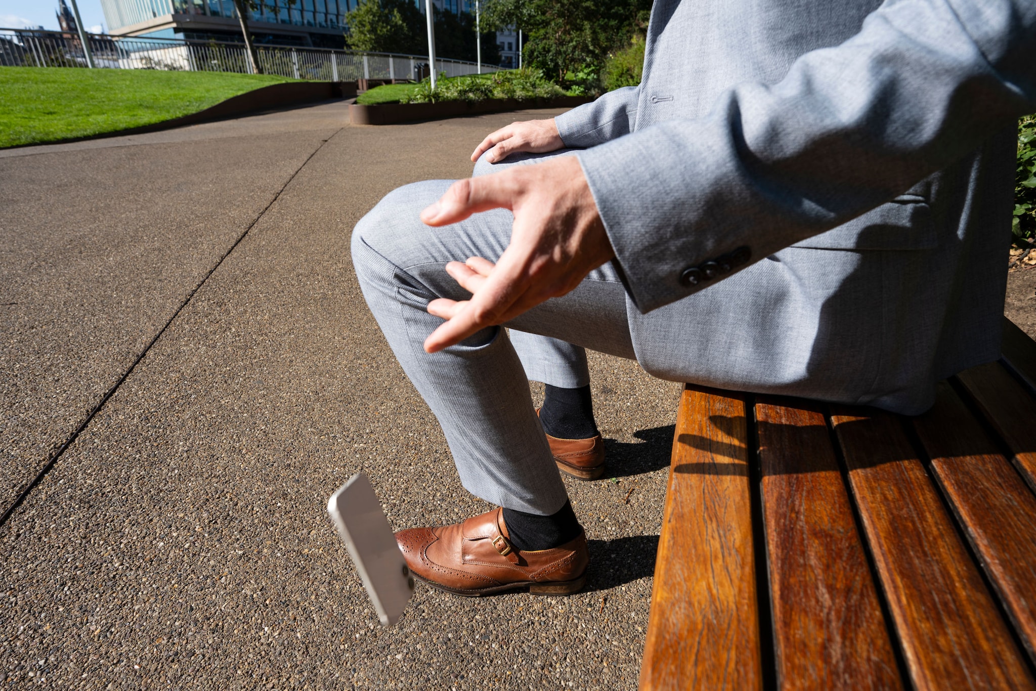 Einem Mann, der auf einer Bank sitzt, fällt sein Smartphone aus der Hand.