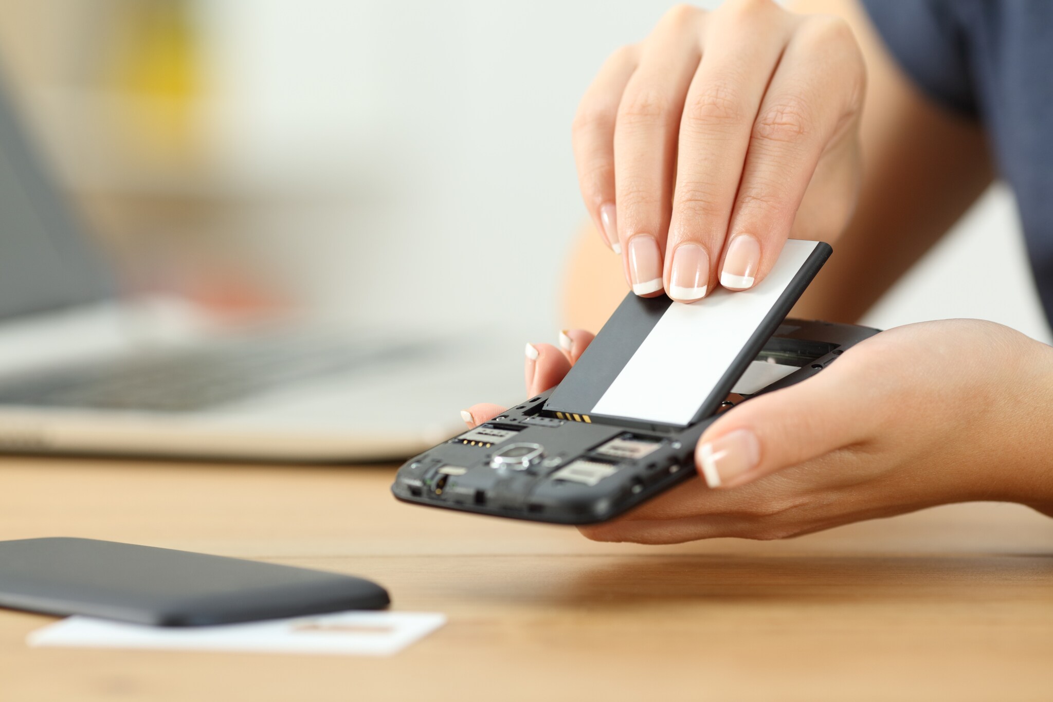 Zu sehen sind die Hände einer Frau, die einen Akku in ein Smartphone steckt.
