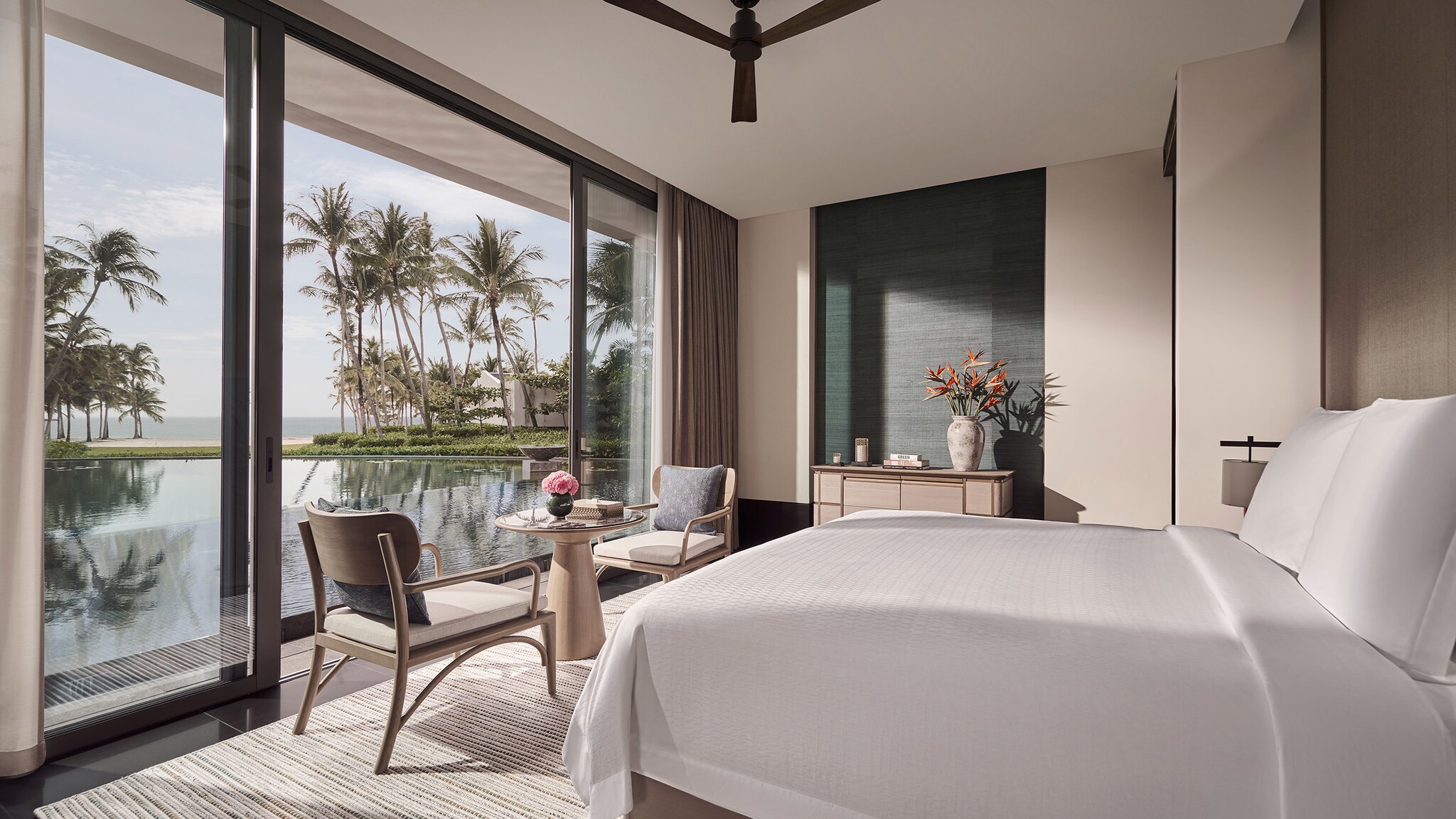 Luxuriöses Hotelzimmer mit Panoramafenster mit Zugang zu einem palmengesäumten Pool am Meer. 