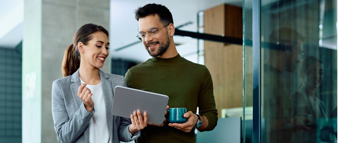 Startseite Coporate Solutions + Peer Learning Eine Frau und ein Mann schauen lächelnd nebeneinanderstehend auf ein Tablet.