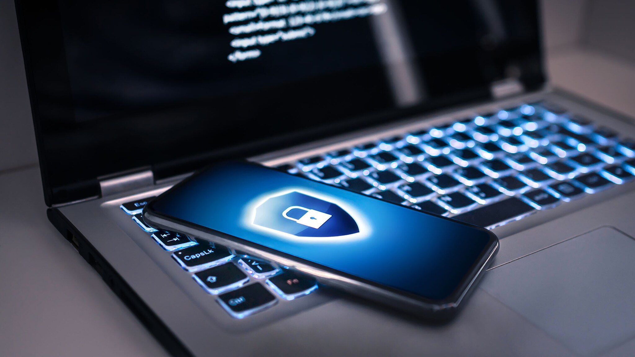 Ein Smartphone mit Sicherheits-Symbol auf dem Display liegt auf einem aufgeklappten Laptop in abgedunkelter Umgebung.