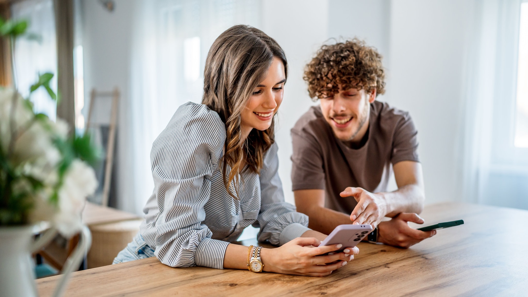 Eine Frau und ein Mann stehen in der Küche und schauen auf ein Smartphone.
