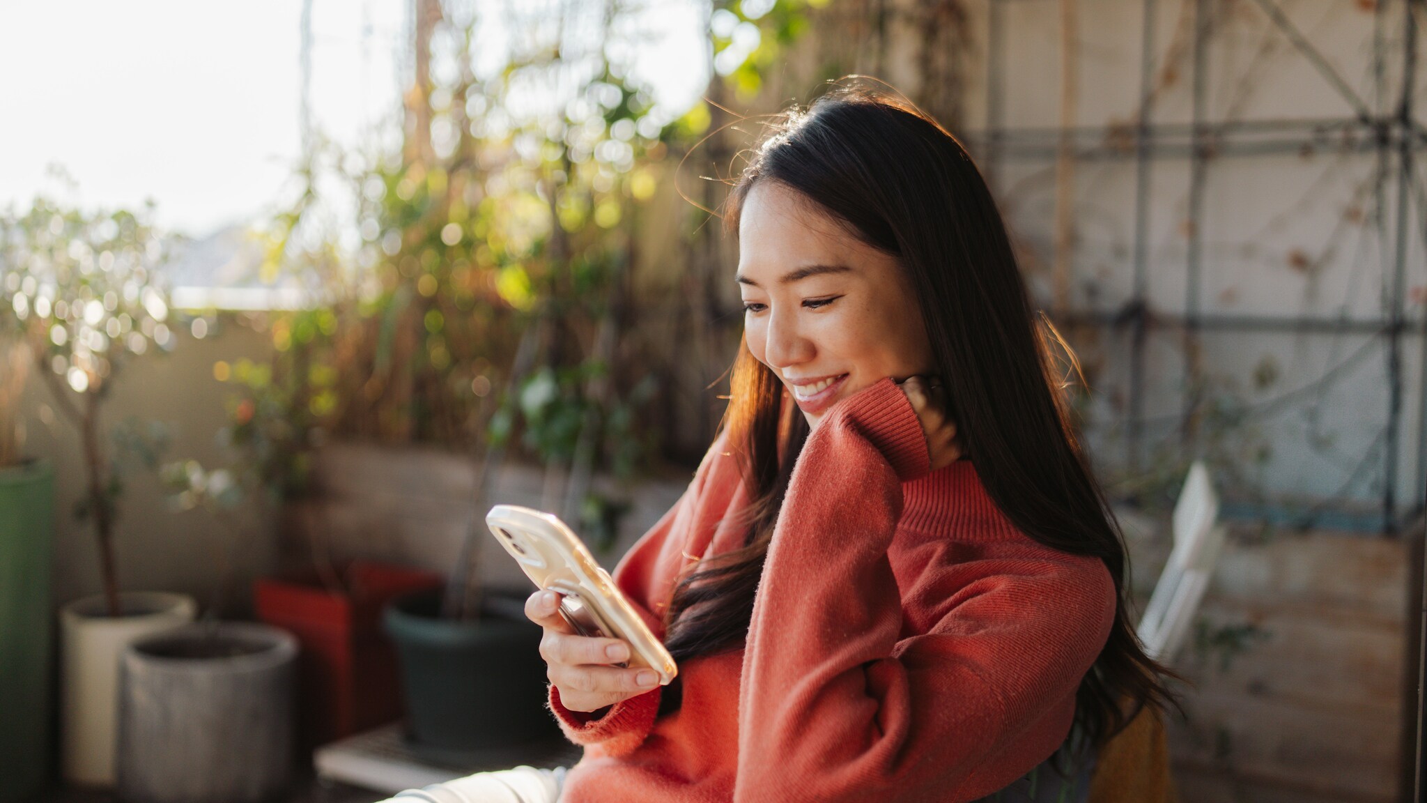 Eine Frau sitzt auf einer Terrasse und schaut auf ihr Smartphone.