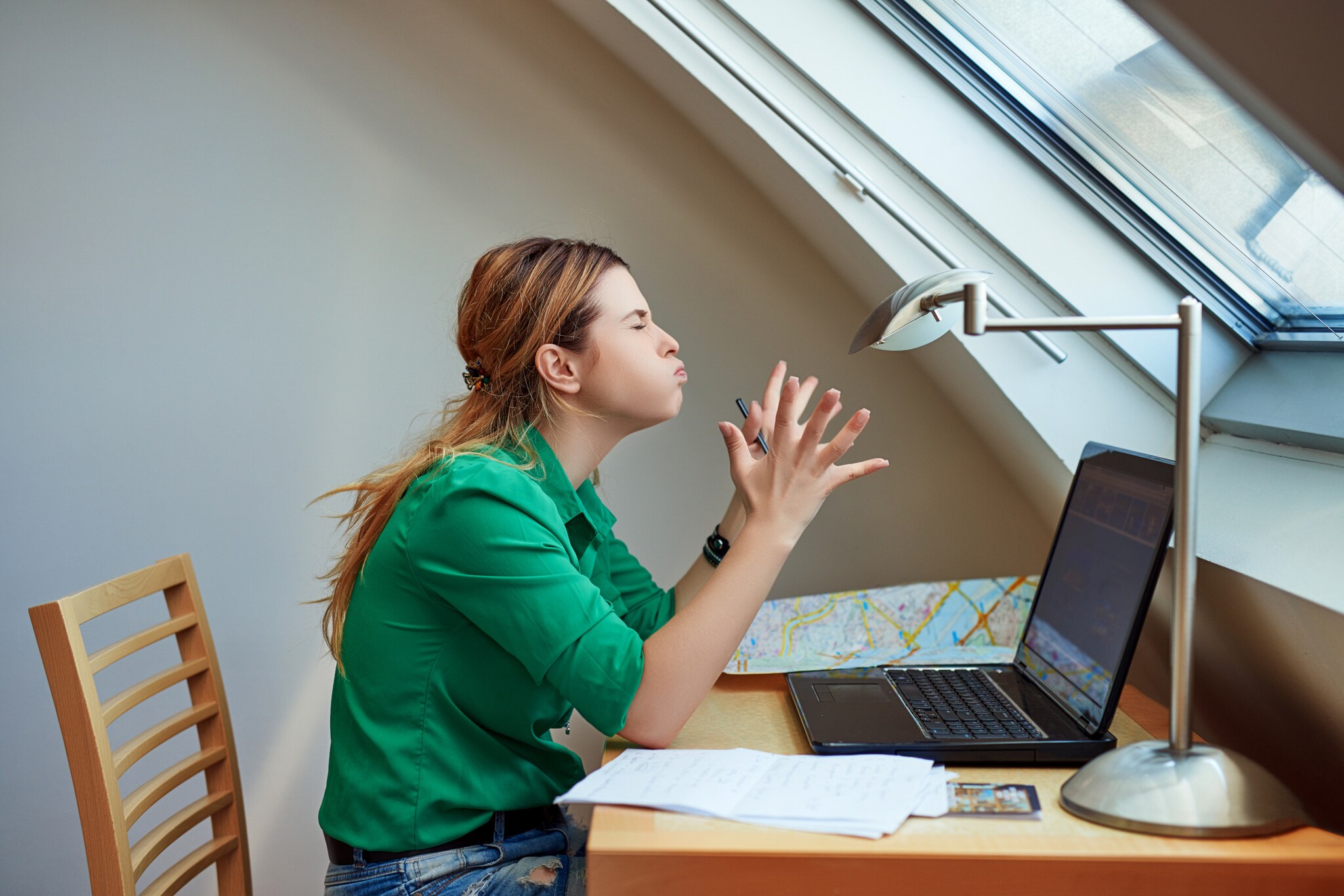 Eine Frau sitzt vor ihrem Laptop, sie hat die Augen geschlossen, einen wütenden Gesichtsausdruck und gestikuliert wild mit ihren Händen. 
