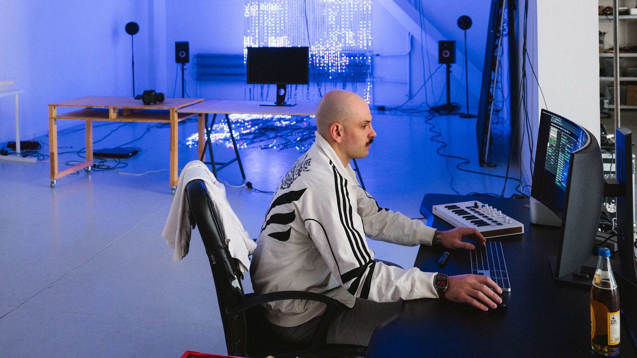 Ein Mann bedient einen Computer an einem Schreibtisch in einem Atelier mit blau leuchtendem LED-Kunstwerk.