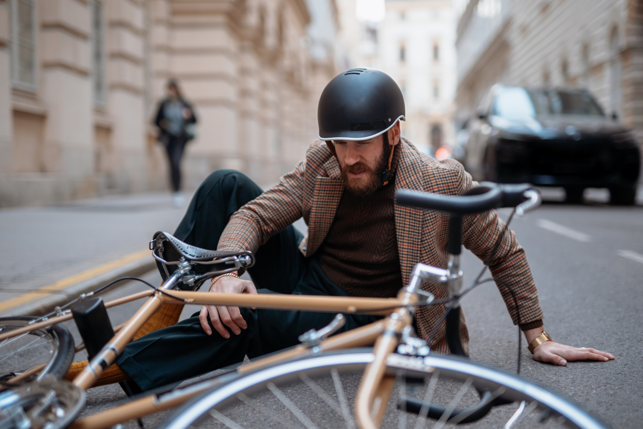 Ein Mann mit Fahrradhelm liegt mit den Beinen unter seinem Fahrrad auf der Straße und hält sich sein Knie.