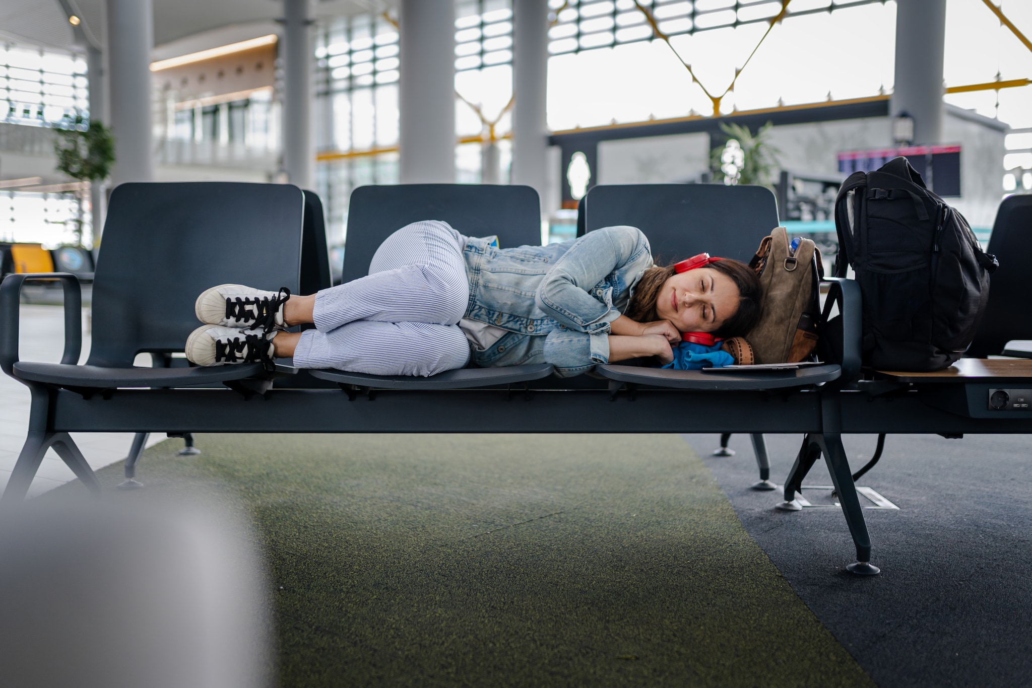 amex-insurance-flug-verspaetet-entschaedigung-frau-sitzbank Eine Frau liegt auf der Seite auf einer Sitzbank im Flughafen.