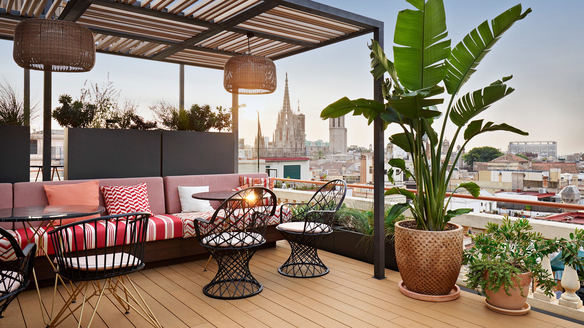 Dachterrasse mit Pflanzen und Sitzgelegenheiten vor Stadtpanorama im Zentrum Barcelonas.
