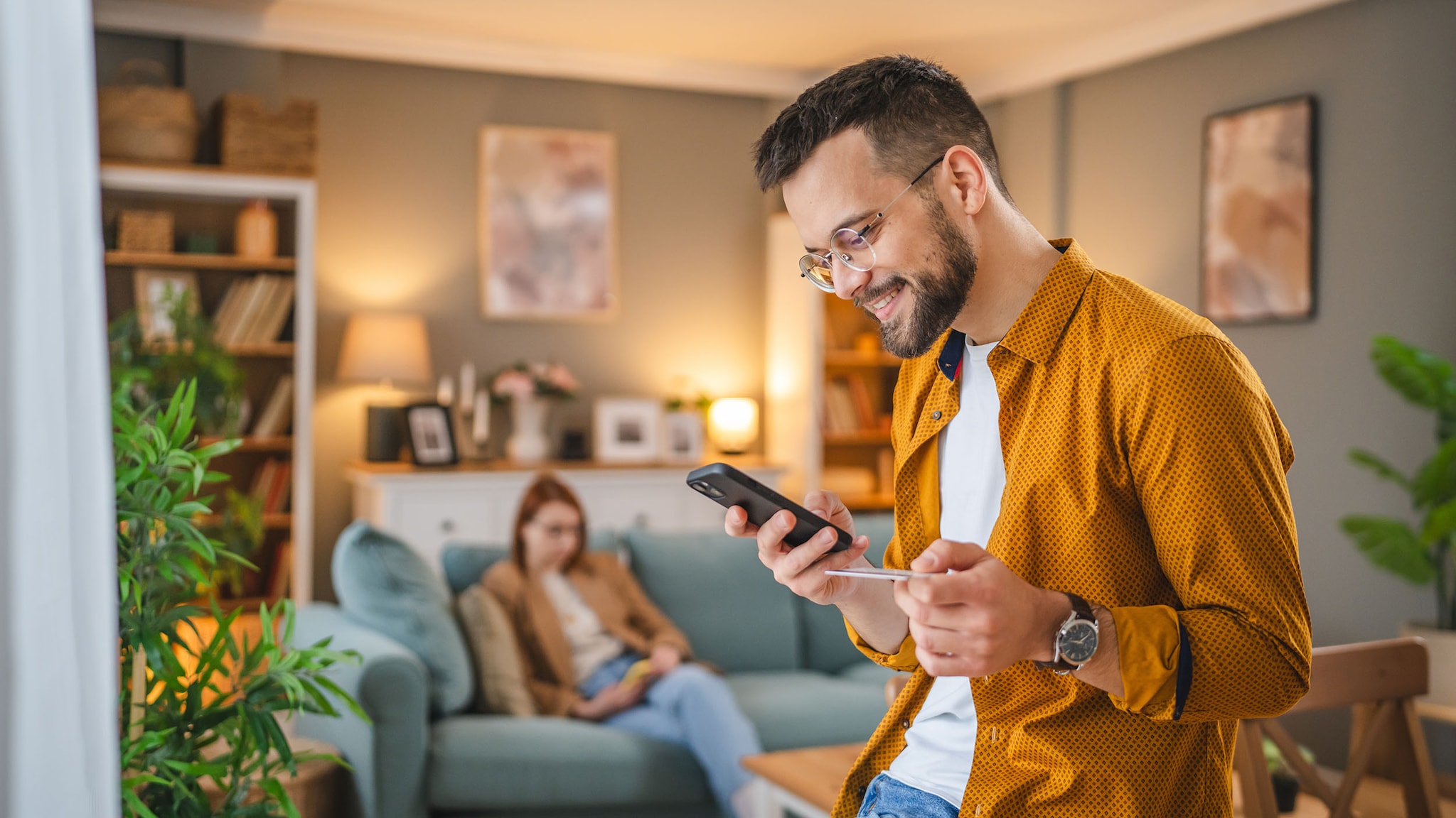 Ein Mann schaut auf sein Smartphone und hält eine Kreditkarte in der Hand.