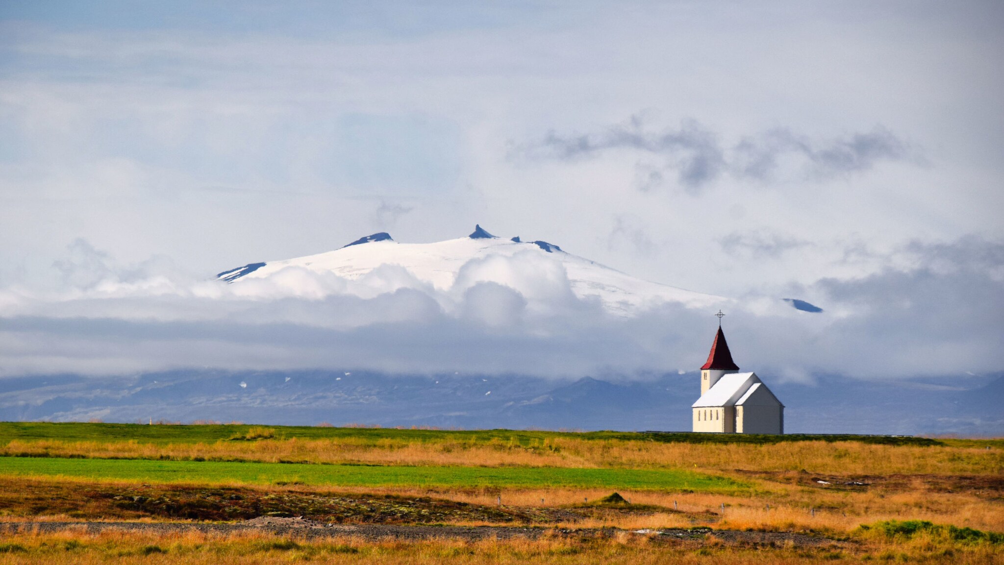 Graslandschaft mit kleiner Kirche vor dem, im Nebel hängenden Gletschervulkan Snæfellsjökull.