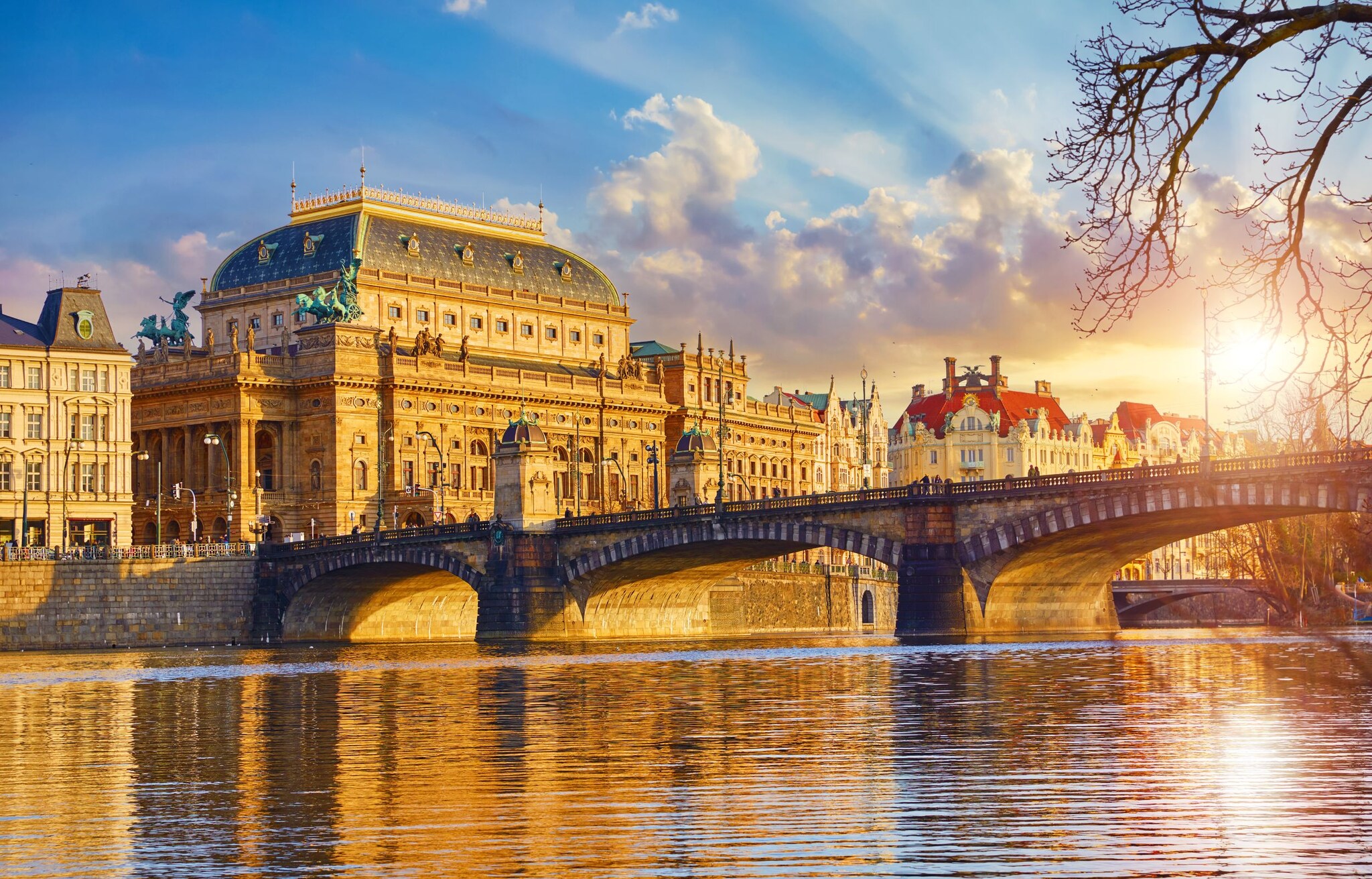 Blick auf prächtige Häuser und eine Brücke über die Moldau in Prag bei Sonnenuntergang.