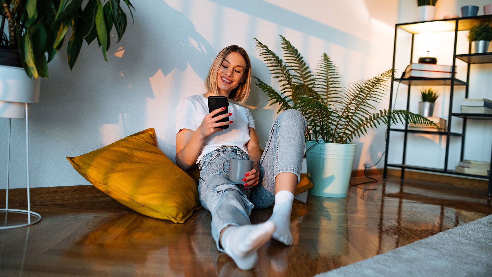 Eine Frau sitzt gemütlich auf dem Boden und schaut in ihr Smartphone.