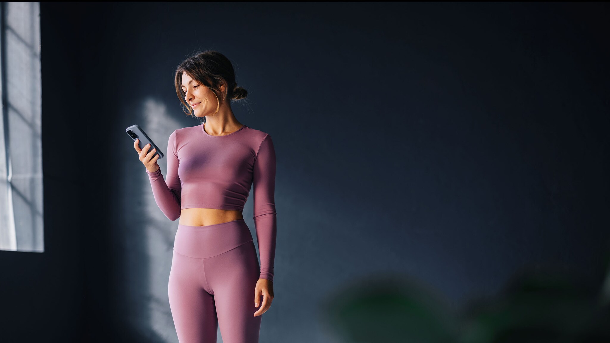 Eine Frau in Yoga-Kleidung schaut auf ihr Smartphone.