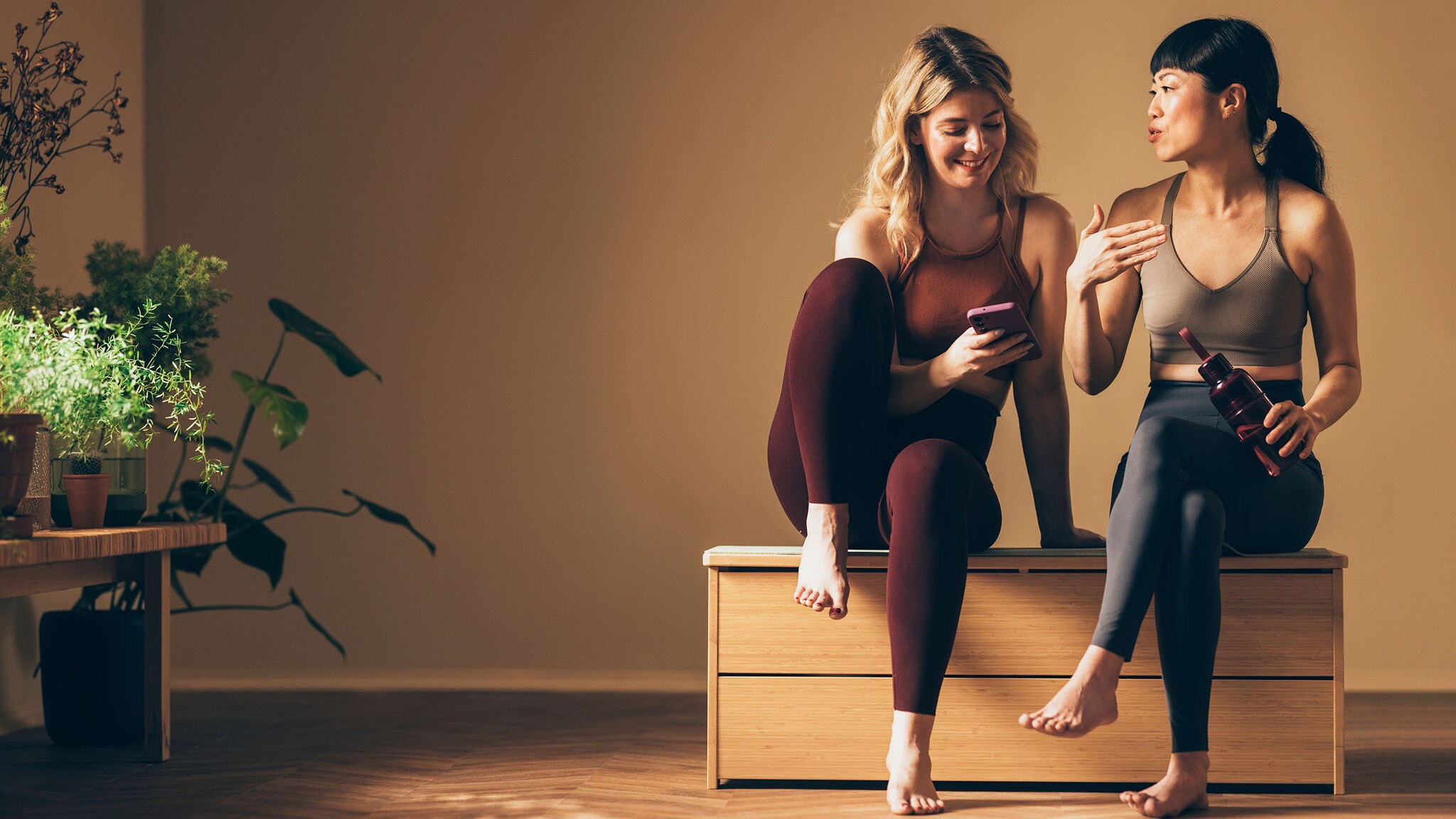 Zwei Frauen in Yoga-Kleidung schauen auf ein Smartphone und unterhalten sich.