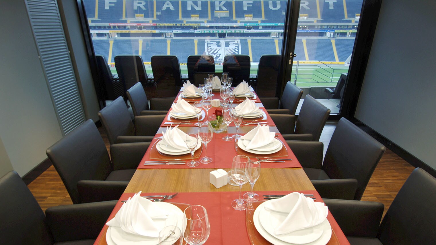 Mehrere Sitzplätze an einem langen, vornehm eingedeckten Tisch in einer Loge in einem menschenleeren Fußballstadion mit Frankfurter Adler-Wappen.
