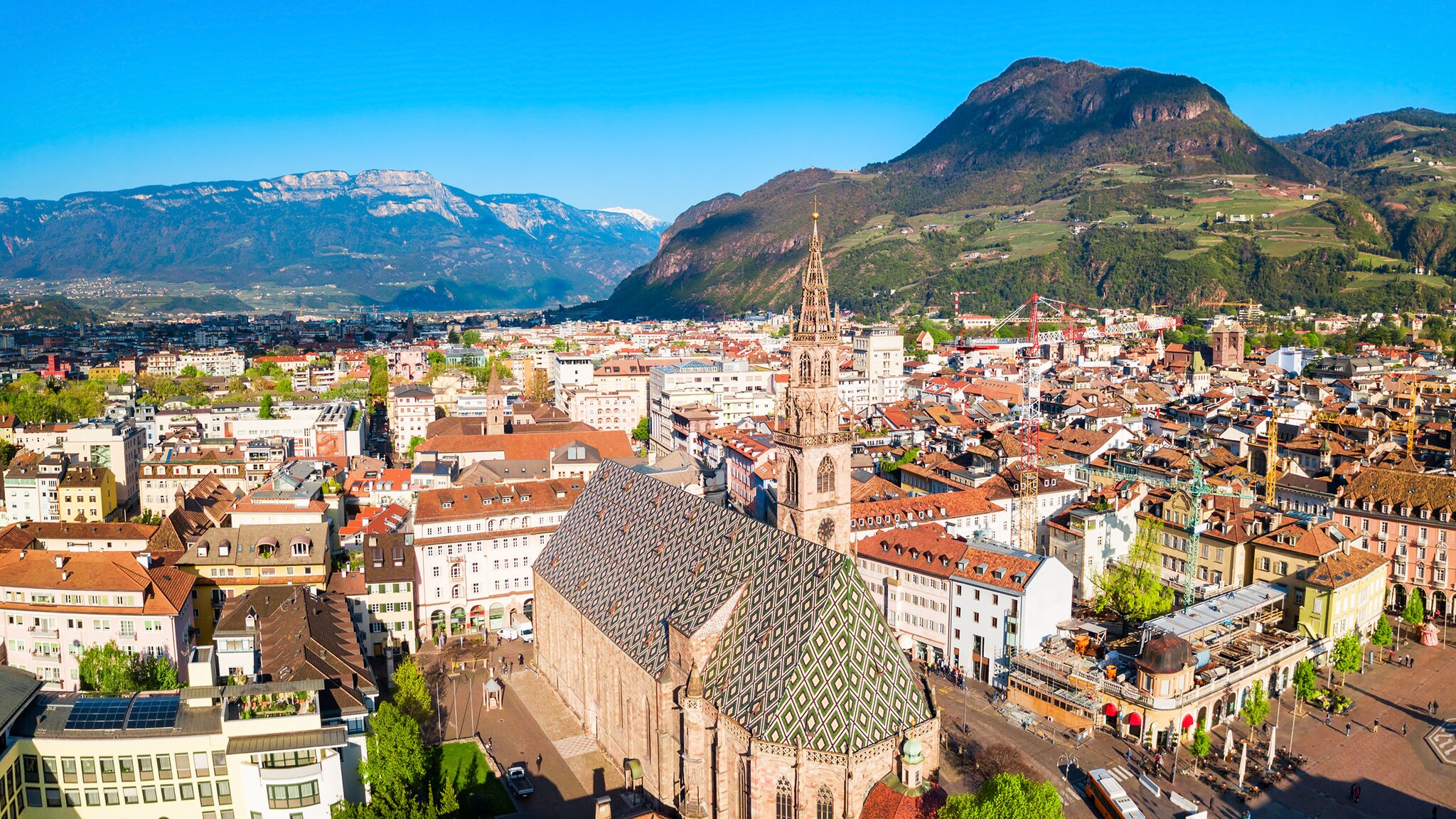 Stadtpanorama von Bozen mit mittelalterlicher Kirche vor Bergpanorama bei Sonnenschein.