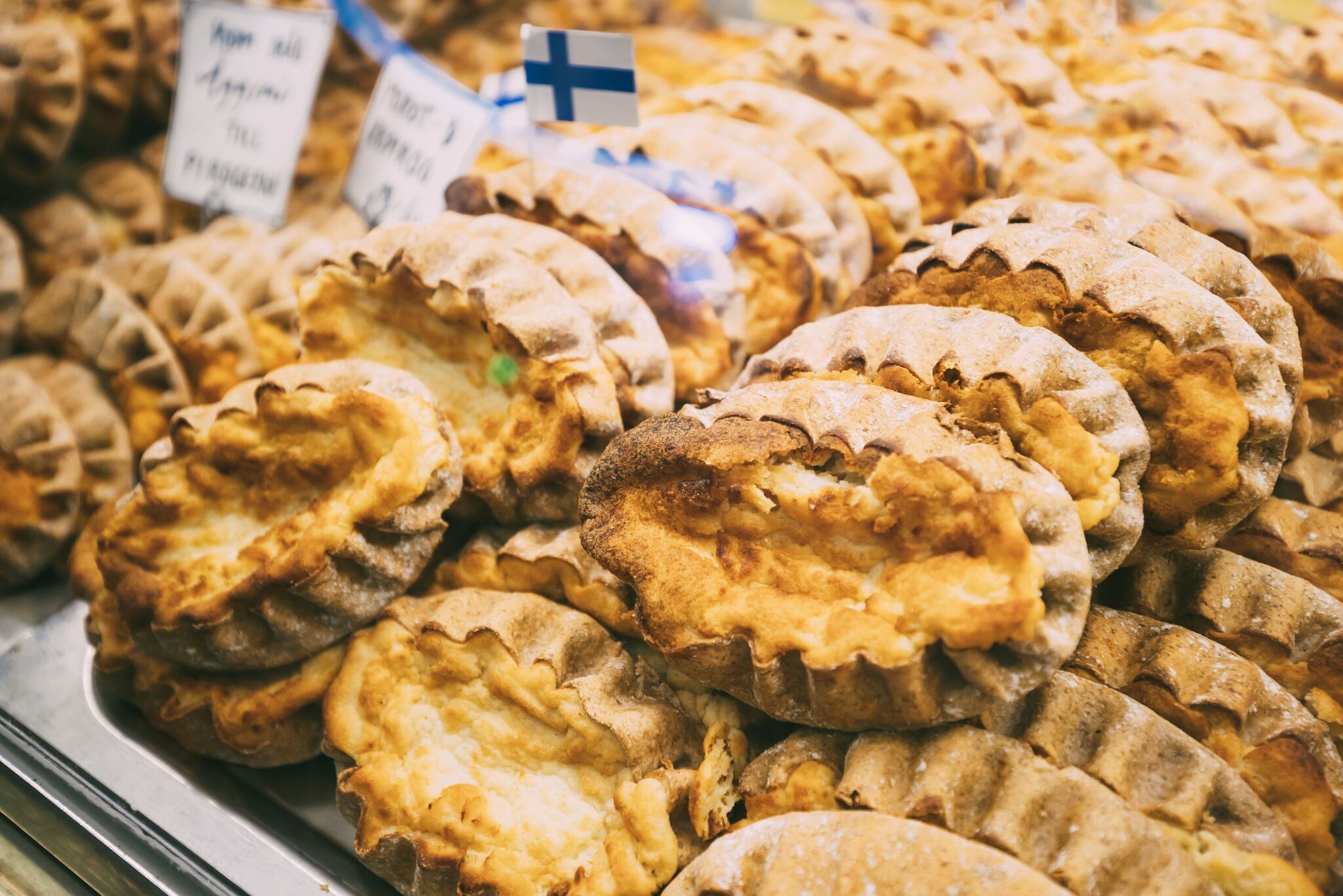 Blick von oben auf ein Blech voller Piroggen aus Roggenteig, zwischendrin beschriebene Schilder und Partypicker mit Finnlandflagge. 