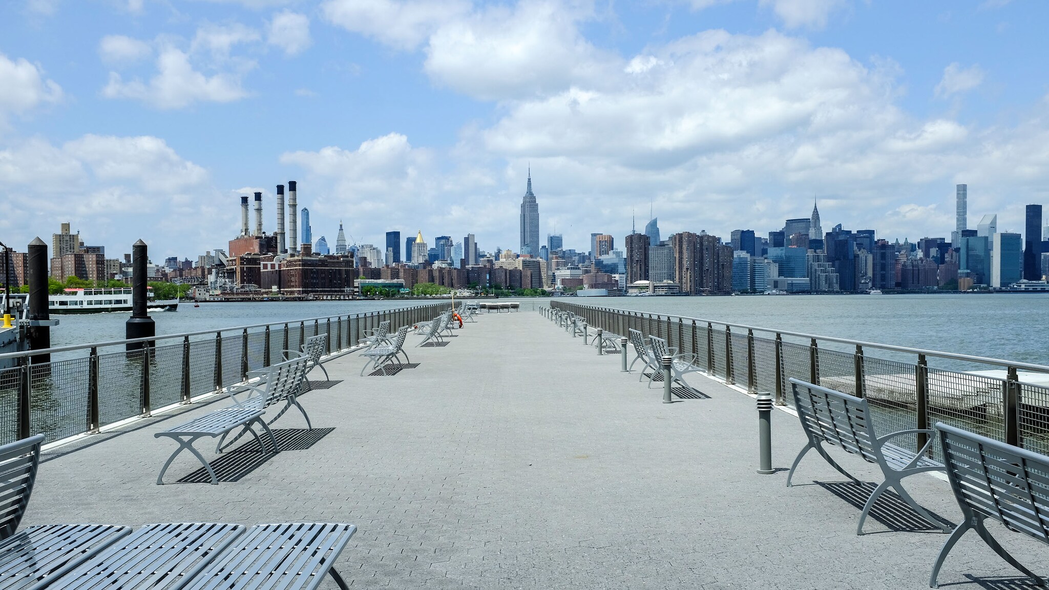 Menschenleerer Pier am Fluss vor der Skyline von Manhattan bei Sonnenschein.