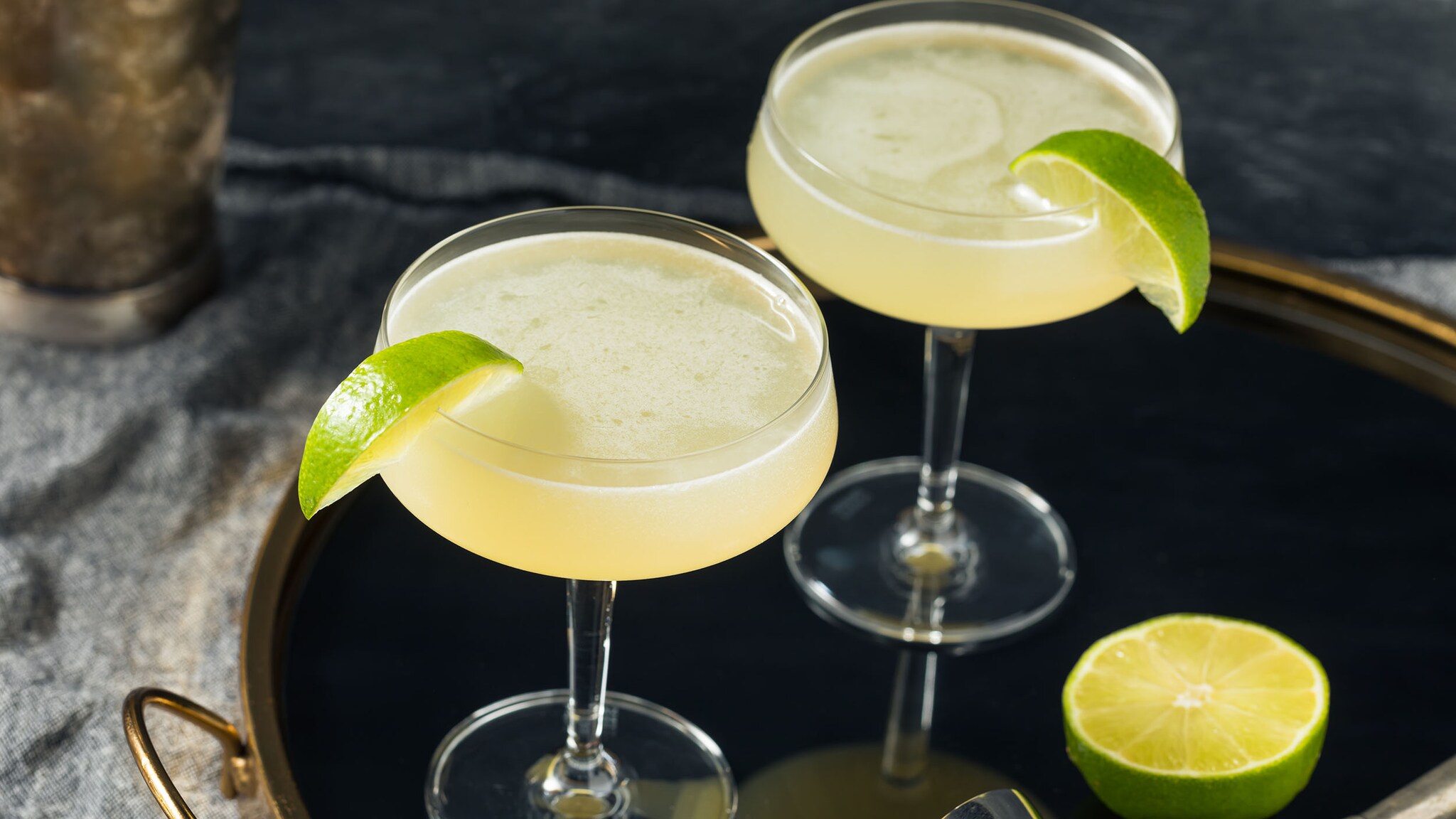 Zwei garnierte, hellgelbe Daiquiris in Cocktailschalen, garniert mit Limettenscheiben, auf einem Tablett.
