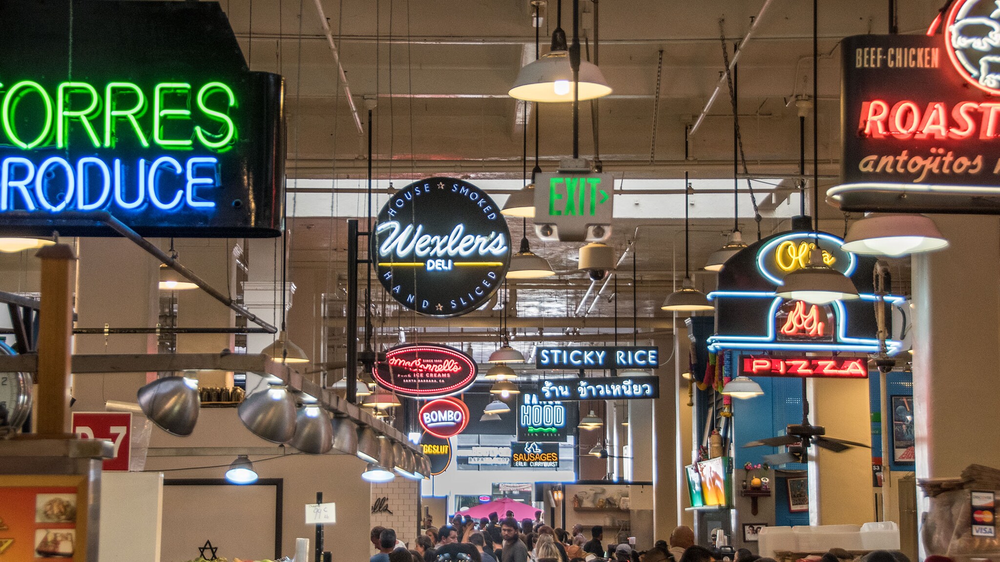 Belebte, überdachte Markthalle mit zahlreichen Neonschildern, die von der Decke hängen.