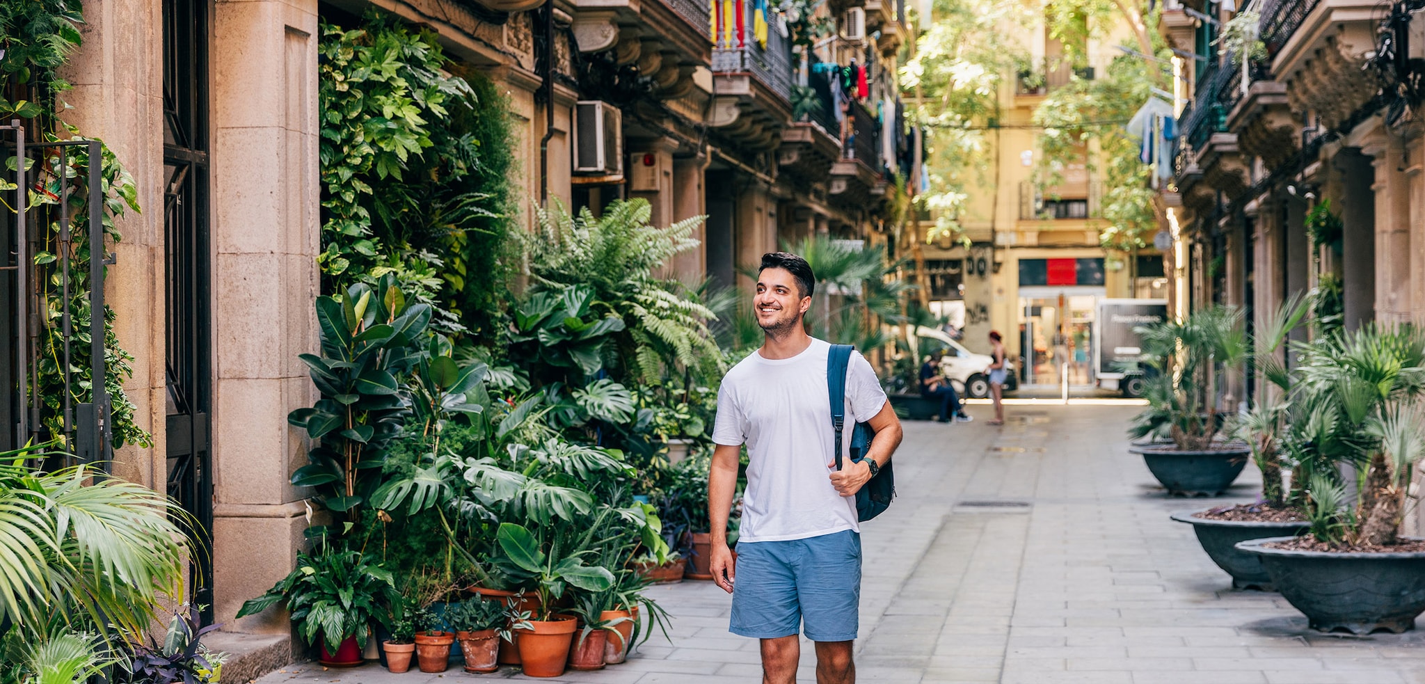 Ein Mann in Sommerkleidung geht durch eine Gasse mit vielen Pflanzen in einer mediterranen Altstadt.