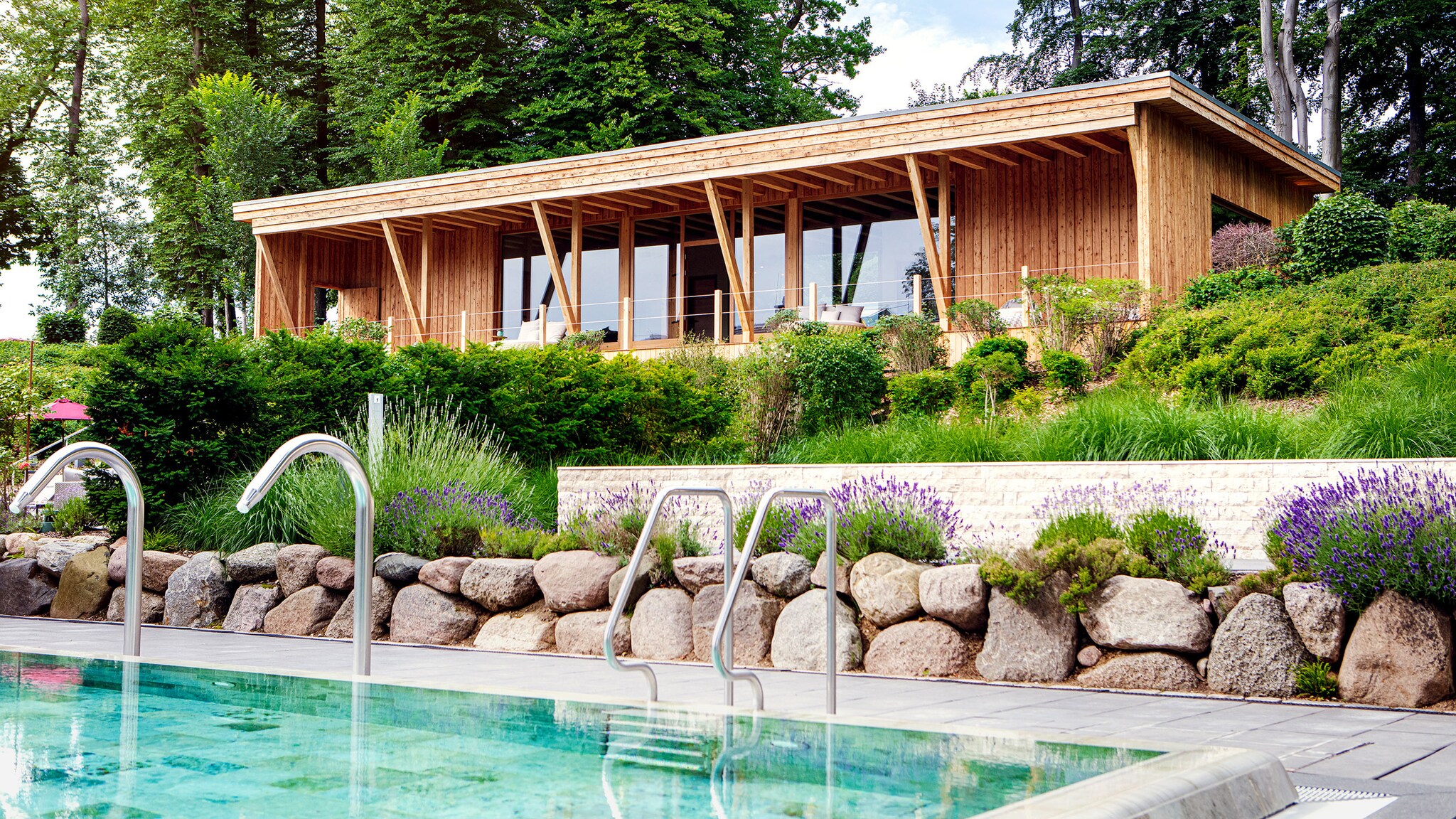 Freistehende Holzsauna in einer Gartenanlage oberhalb eines Pools.