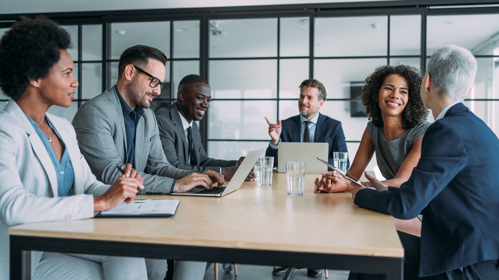 Ein sechsköpfiges Business-Team kommuniziert entspannt und gut gelaunt an einem Konferenztisch im Büro.