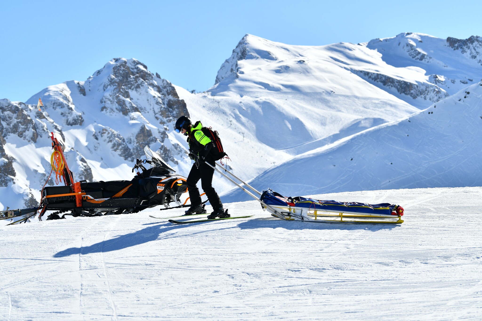 Eine Person auf einem Rettungsschlitten wird von einem Bergretter zu einem Rettungsmobil durch den Schnee gezogen.