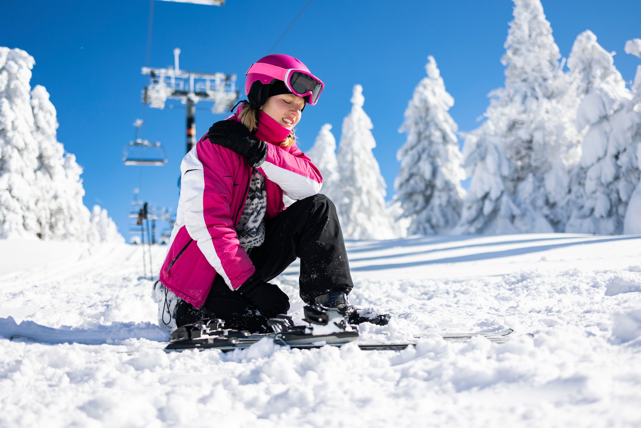 amex-insurance-skiunfall-skifahrerin Eine Skifahrerin sitzt mit schmerzverzerrtem Gesicht auf der Piste im Schnee und hält sich die Schulter.