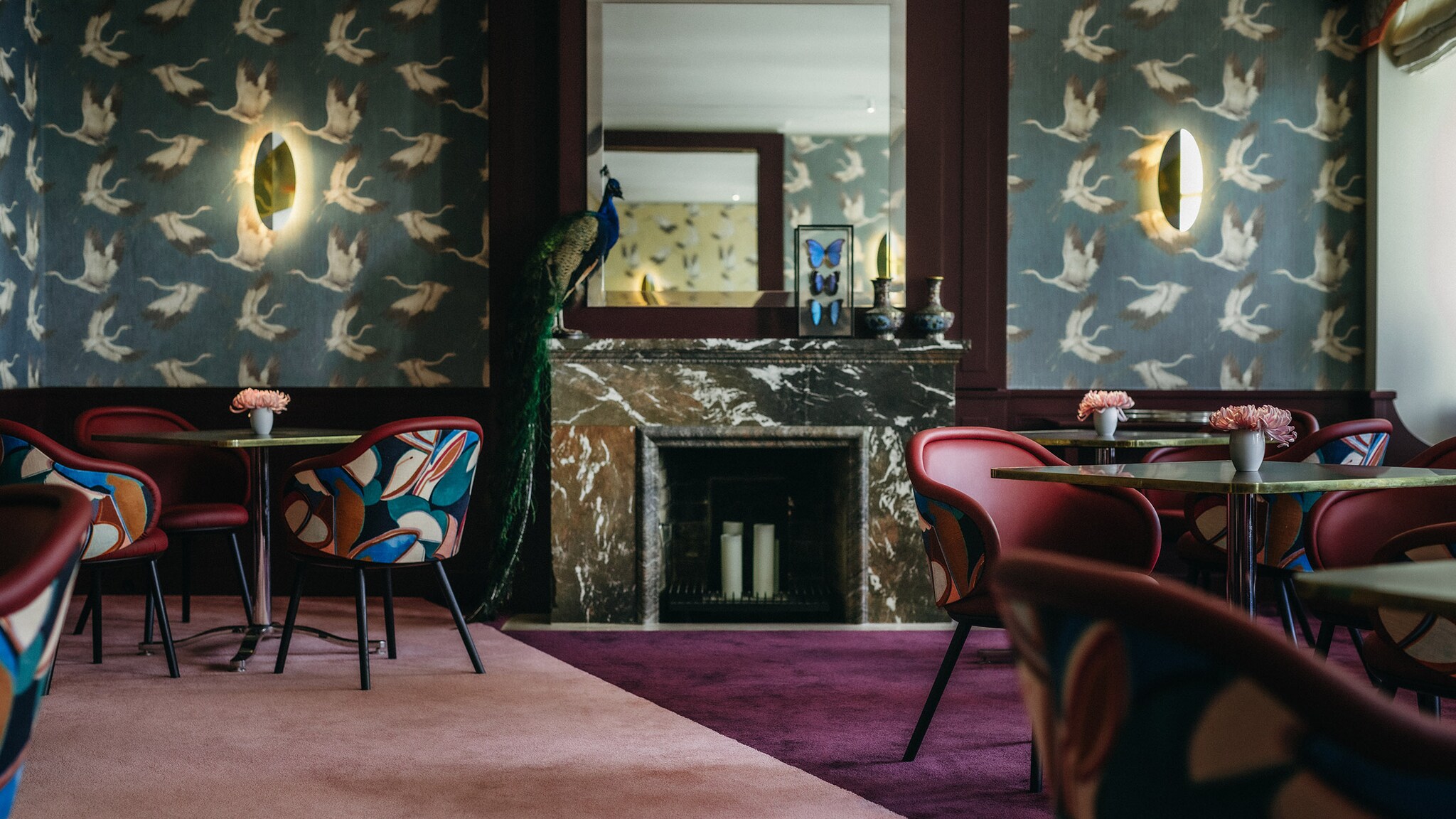 Speisesaal mit stilvollem Interieur mit einer mit Kranichen gemusterten Tapete und einem ausgestopften Pfau auf einem Kaminsims.