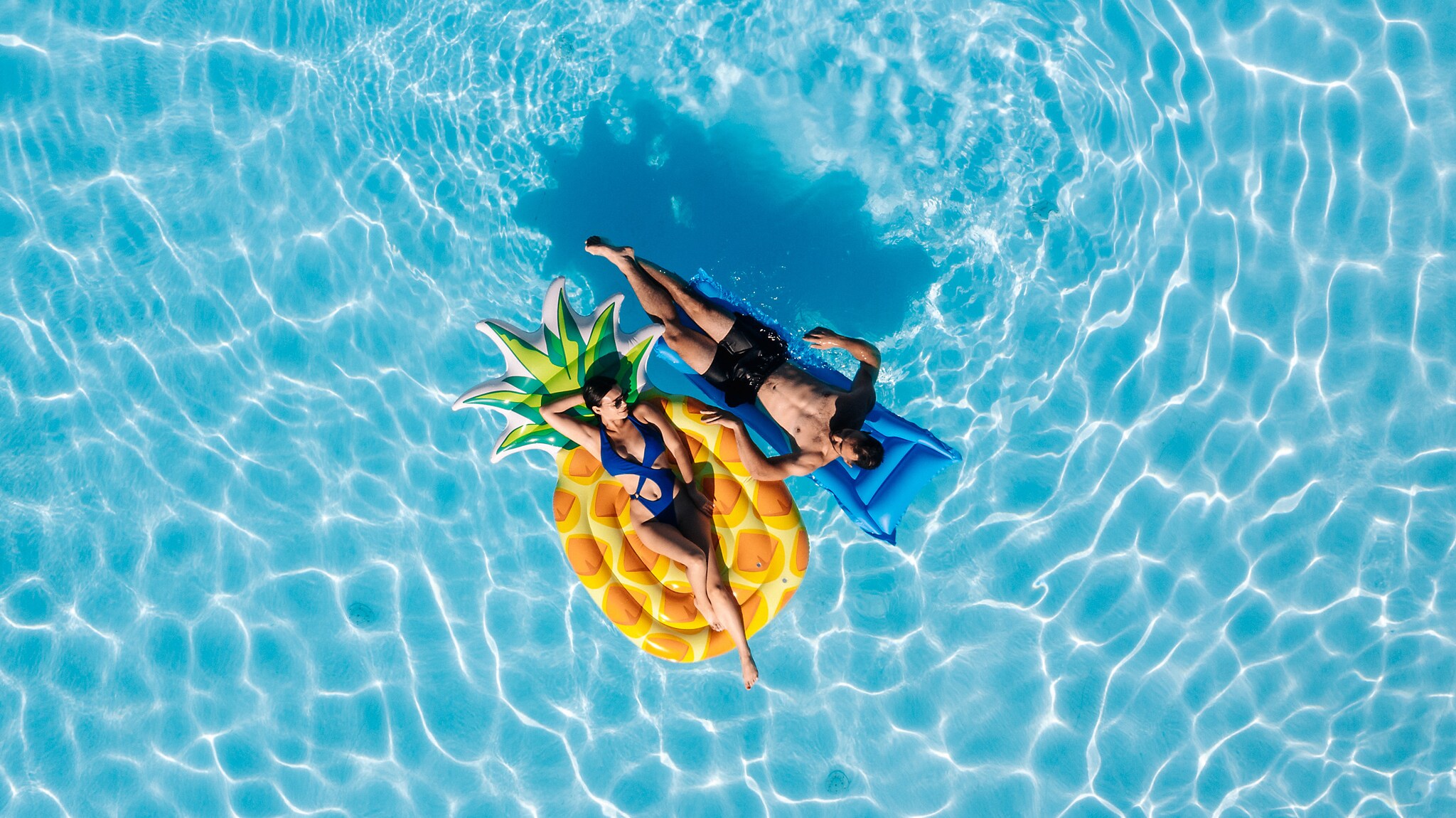 Ein Pärchen liegt auf zwei Luftmatratzen entspannt im Pool.