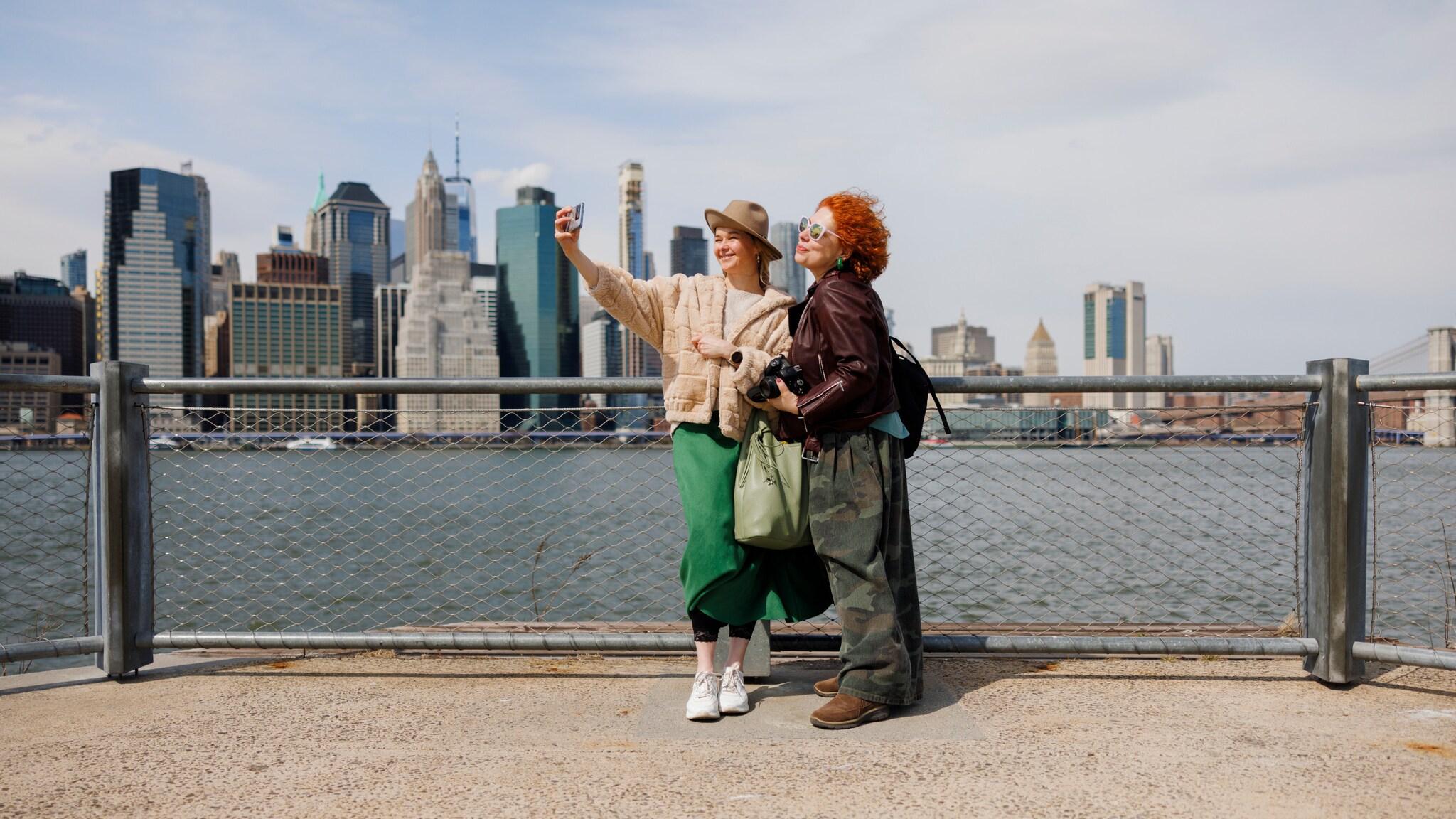 Zwei Frauen machen ein Selfie, im Hintergrund ist die Skyline von Manhatten zu sehen.