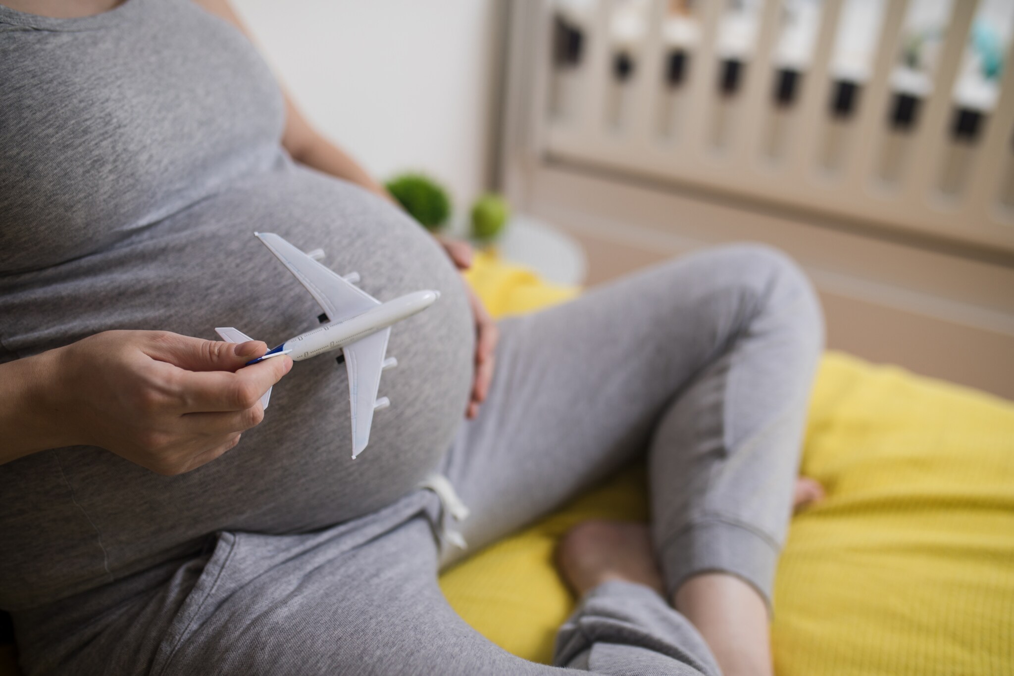 Eine schwangere Person hält ein kleines Plastikflugzeug vor ihren Bauch.