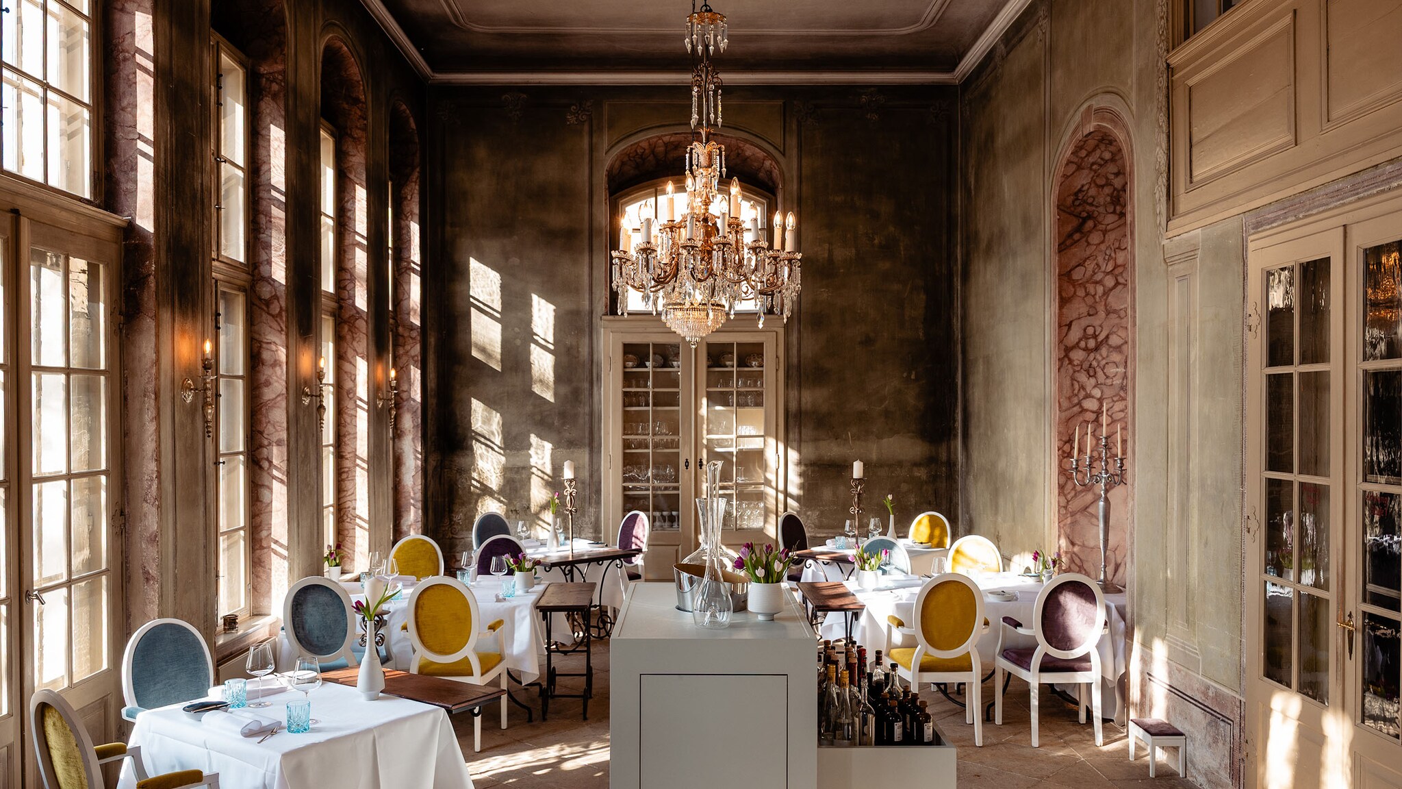 In einem Restaurant stehen Möbel im Barockstil, unter der Stuckdecke hängt ein Kronleuchter.