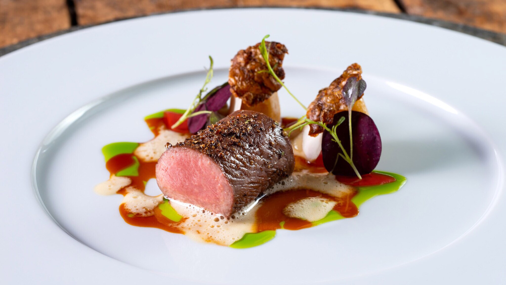 Ein Stück Fleisch mit Garnierung und Soße auf einem weißen Teller