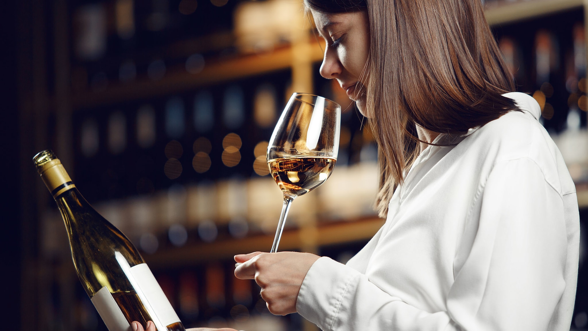 Eine Frau hält eine Weinflasche in der Hand und riecht an einem Glas Weißwein