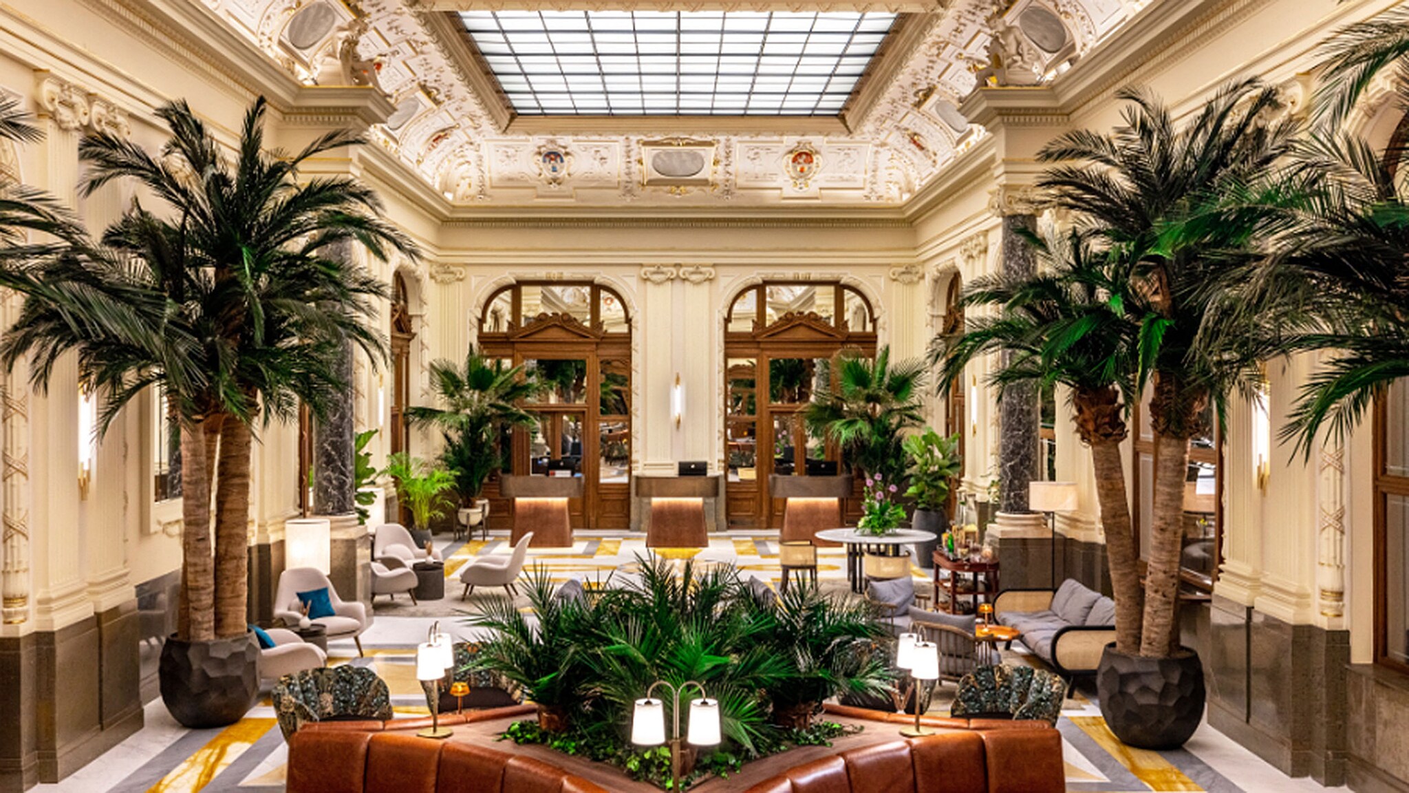 Elegante Hotellobby im Neorenaissance-Stil mit Sitzgelegenheiten zwischen Palmen.