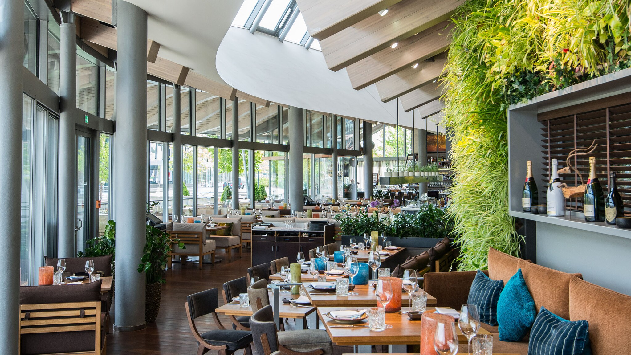 In einem Restaurant mit großer Fensterfront stehen gedeckte Tische mit Stühlen und Sofas.
