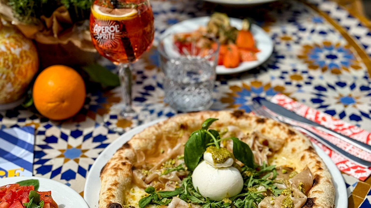  In einem Restaurant steht eine Pizza mit Burrata auf einem bunten Tisch.