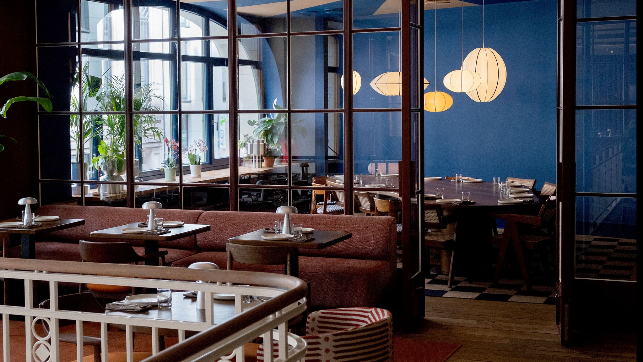 In einem Restaurant mit vielen Sprossenfenstern stehen gedeckte Tische mit Stühlen.