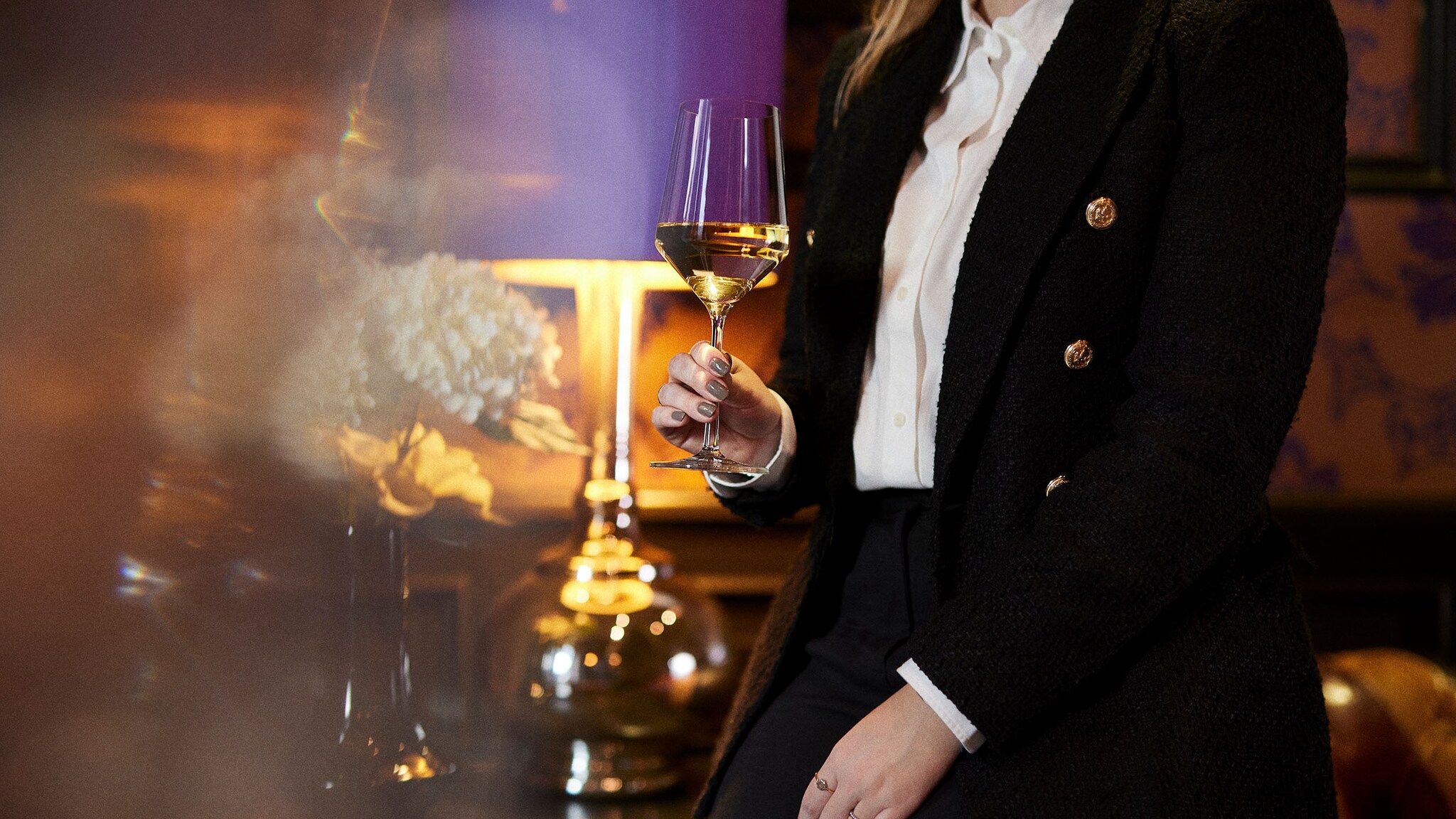 Eine Frau vor einer lilafarbenen Lampe und hält ein Glas Wein in der Hand.