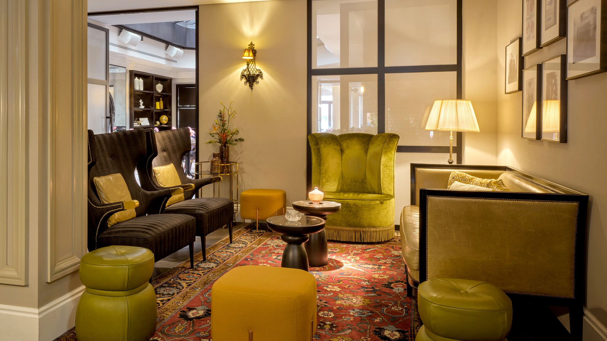 In einer Hotellobby stehen verschiedene Stühle und Hocker aus Samt um einen Perserteppich.