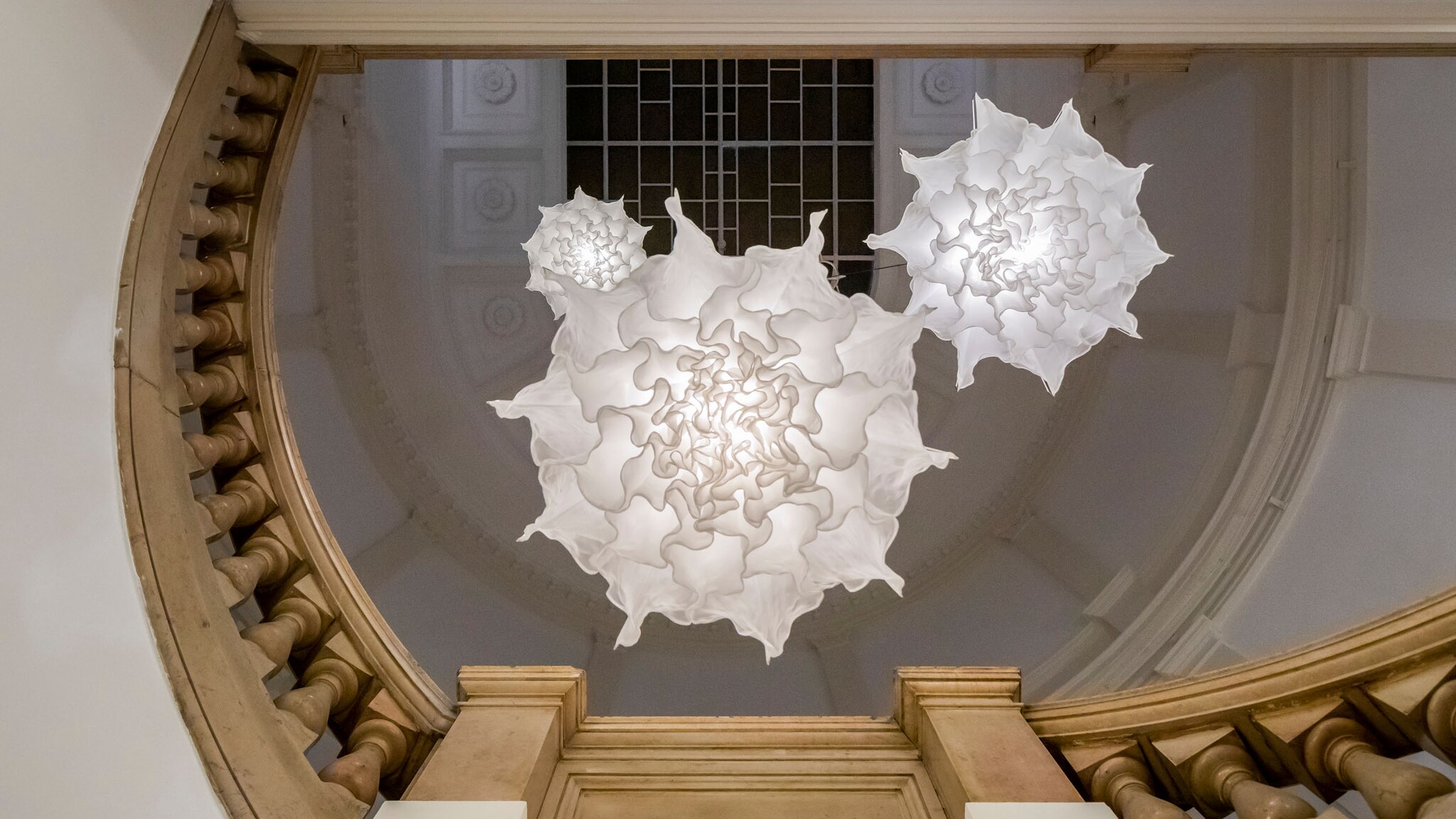 An der Decke in einem historischen Gebäude hängen drei Lampen aus weißem Stoff. 