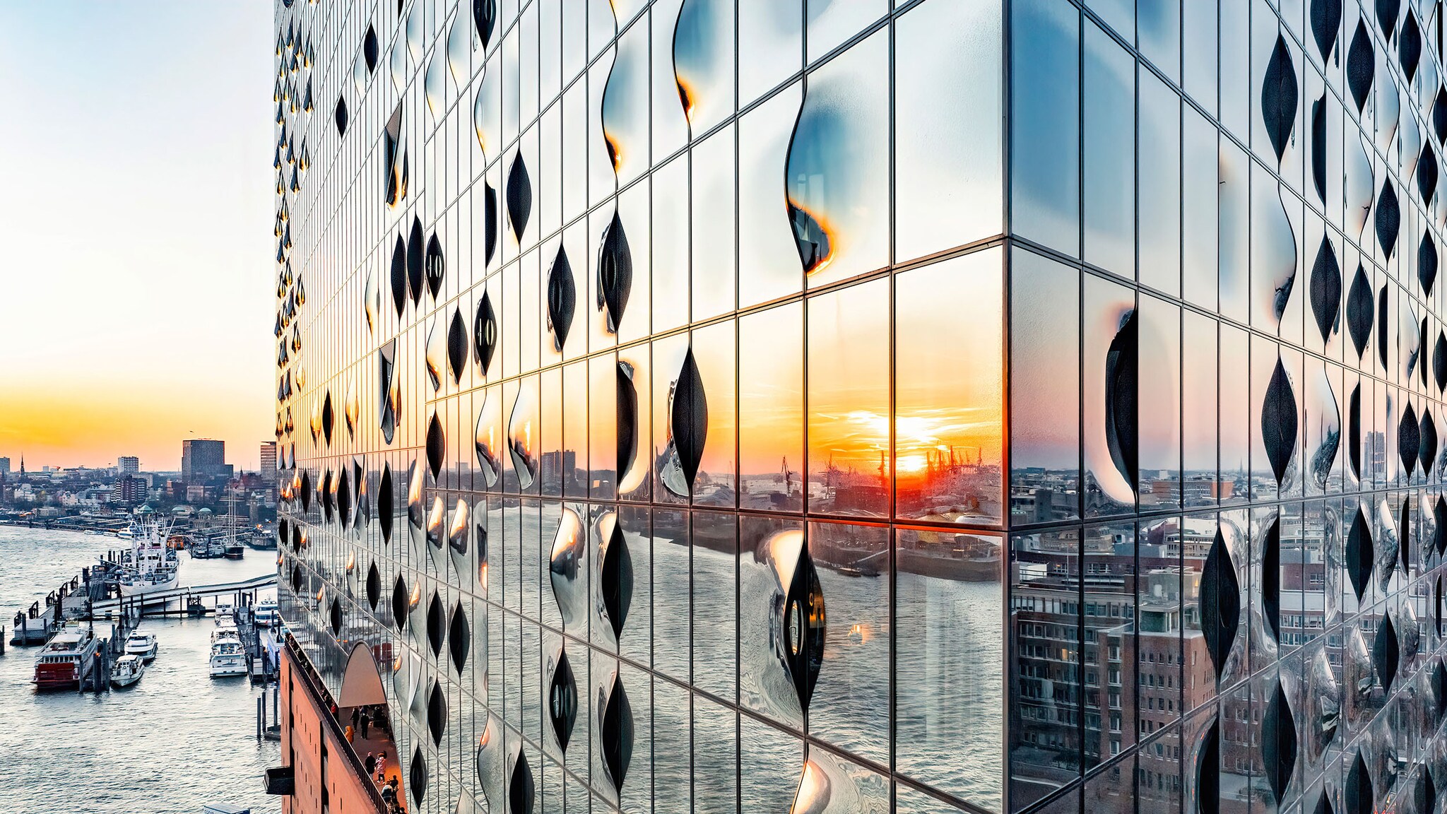 In einem Gebäude mit Glasfasade spiegelt sich der Hafen und Gebäude der Stadt.