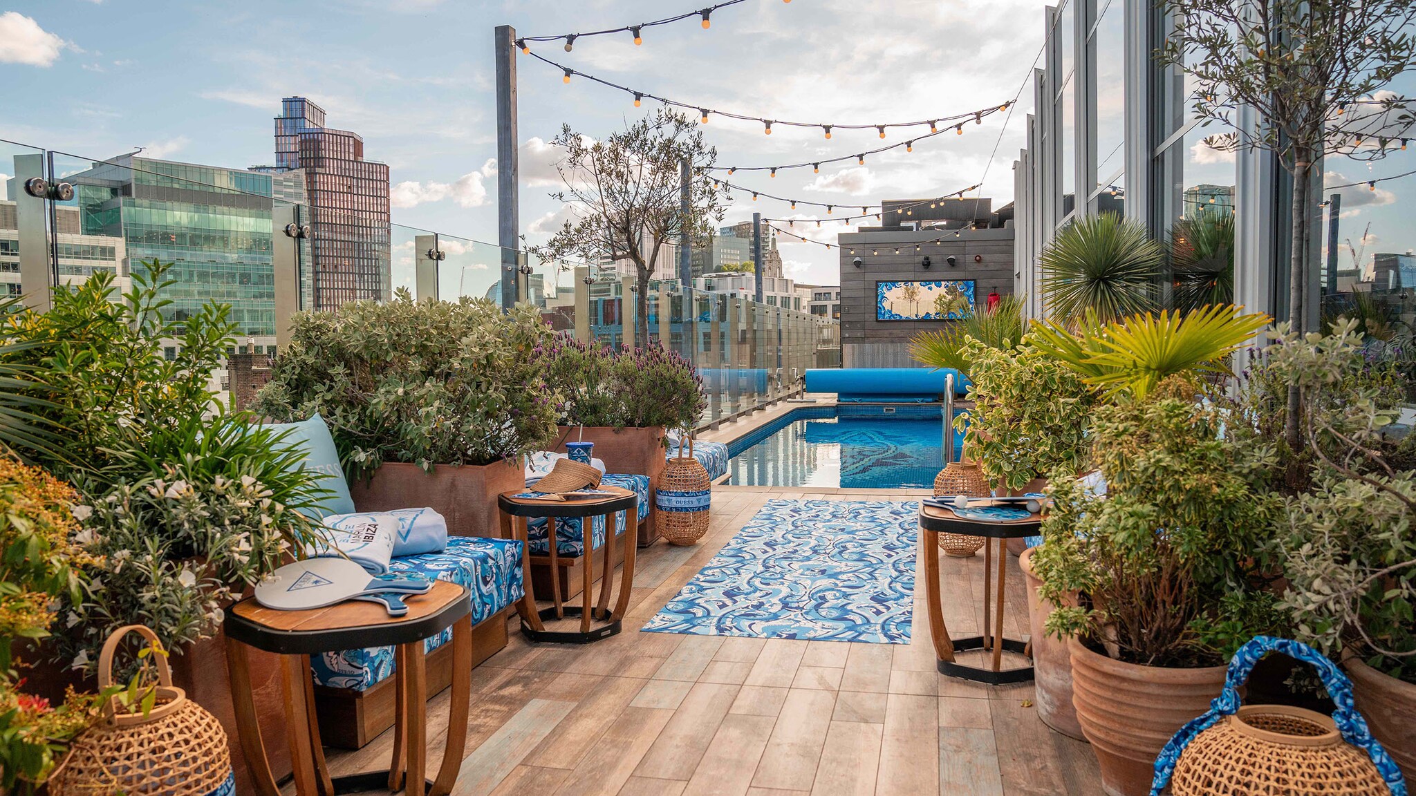 Luxuriöse, stilvolle Dachterrasse mit Pool und Sitzgelegenheiten zwischen zahlreichen Pflanzenkübeln vor der Skyline von London. 
