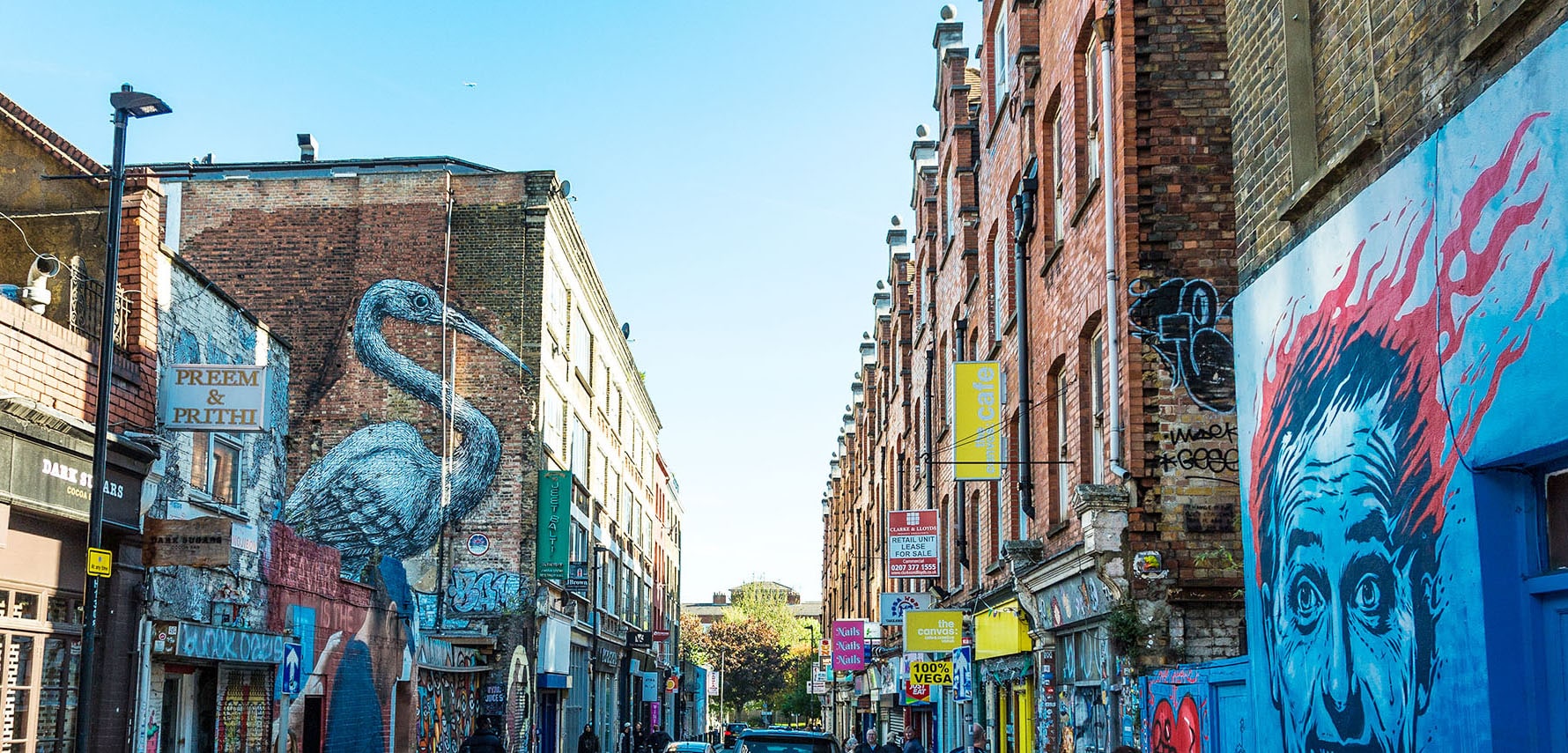 Schmale Straße mit Backsteinhäusern mit Graffiti und Schildern von kleinen Geschäften.